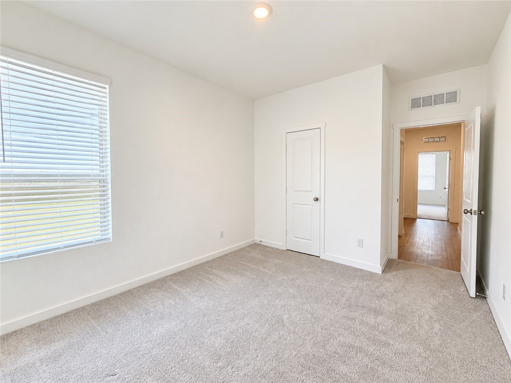 Empty carpeted bedroom with a window and an open doorway to the hall.
