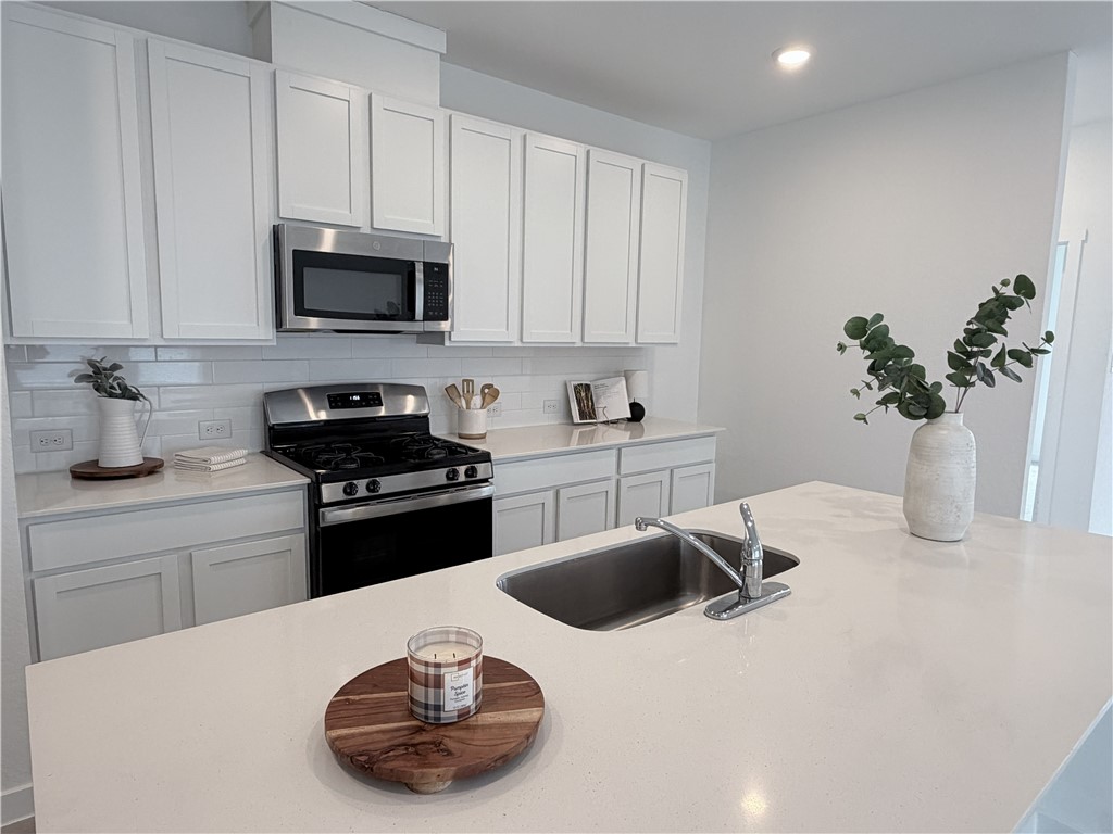 Bright white kitchen with a large island, undermount sink, and stainless steel range and microwave.