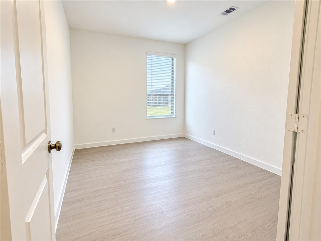 Empty room with light wood-look flooring, white walls, and a window with blinds.