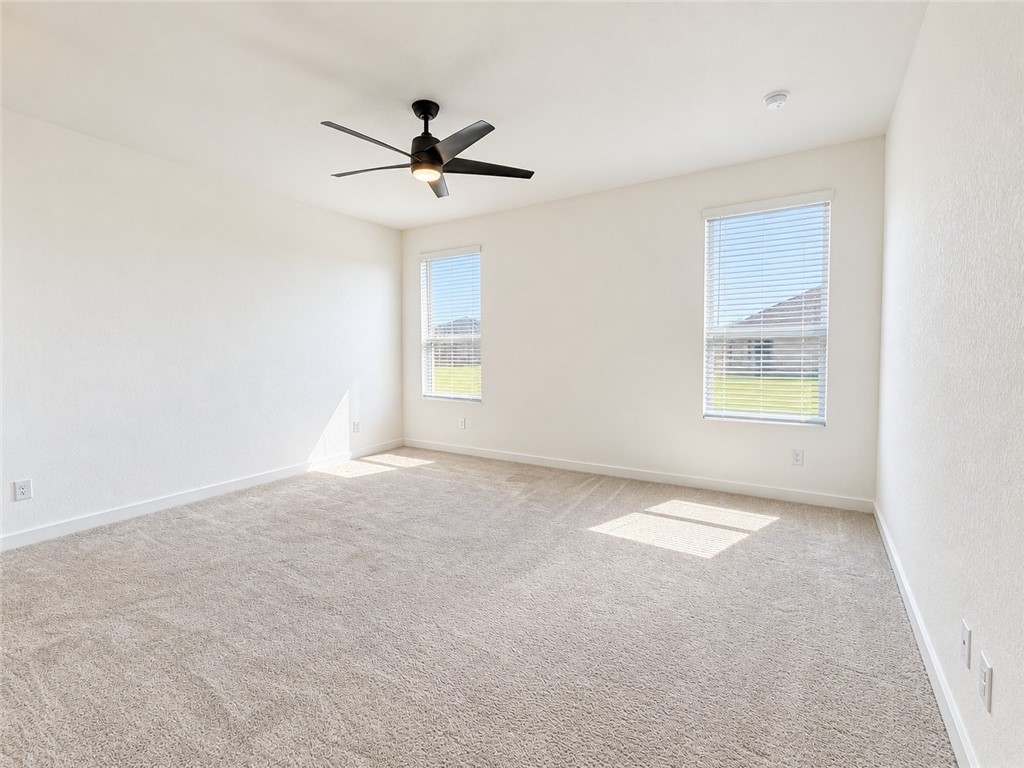 Empty carpeted room with two windows and a ceiling fan.