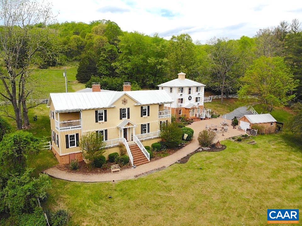 Aerial view of a yellow two-story home with white porches, a patio, and a small outbuilding.