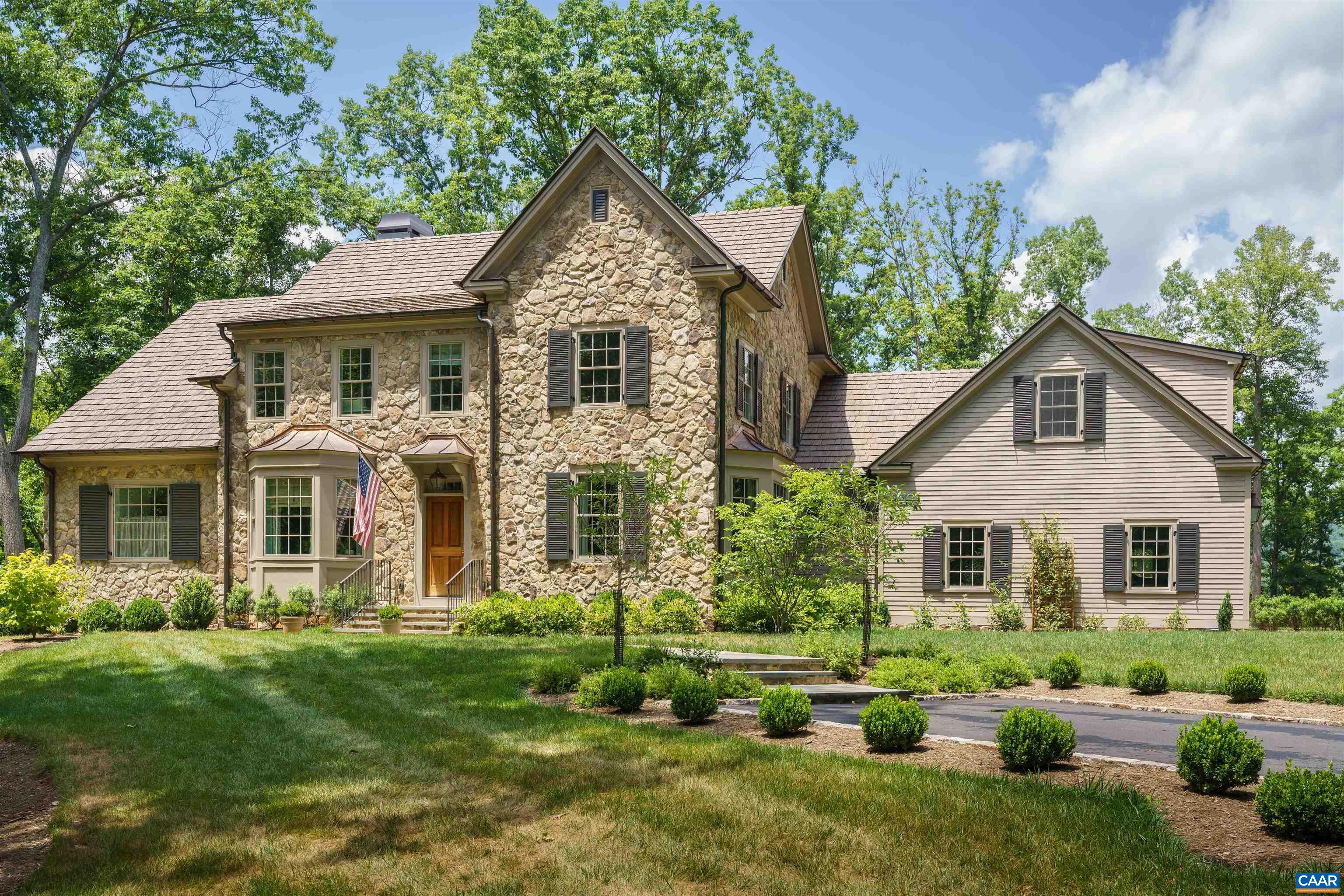 Two-story stone home with a light-sided wing, landscaped lawn, and American flag by the entrance.