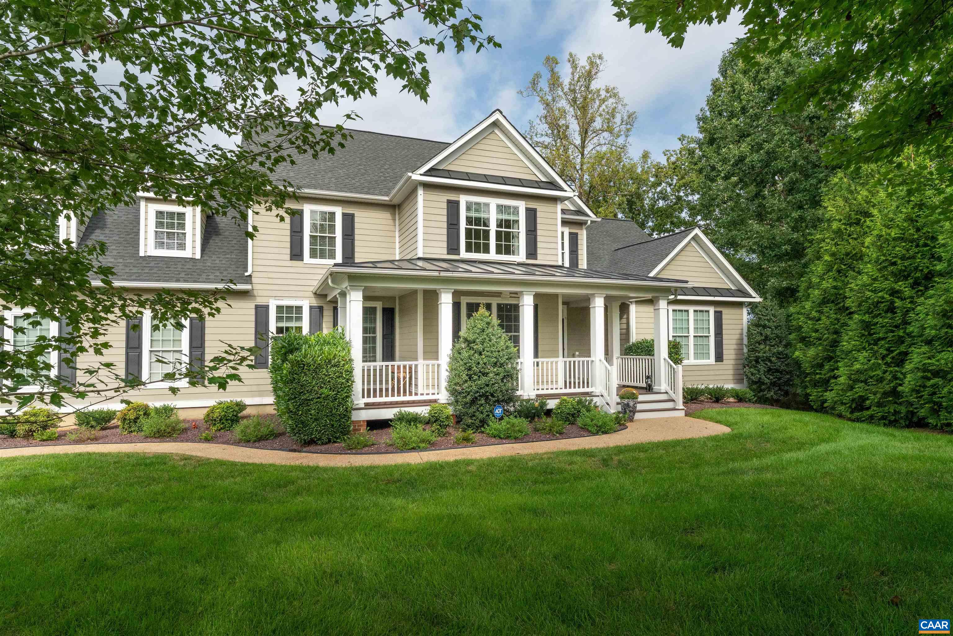 Beige two-story house with a columned front porch, landscaped walkway, and mature trees.
