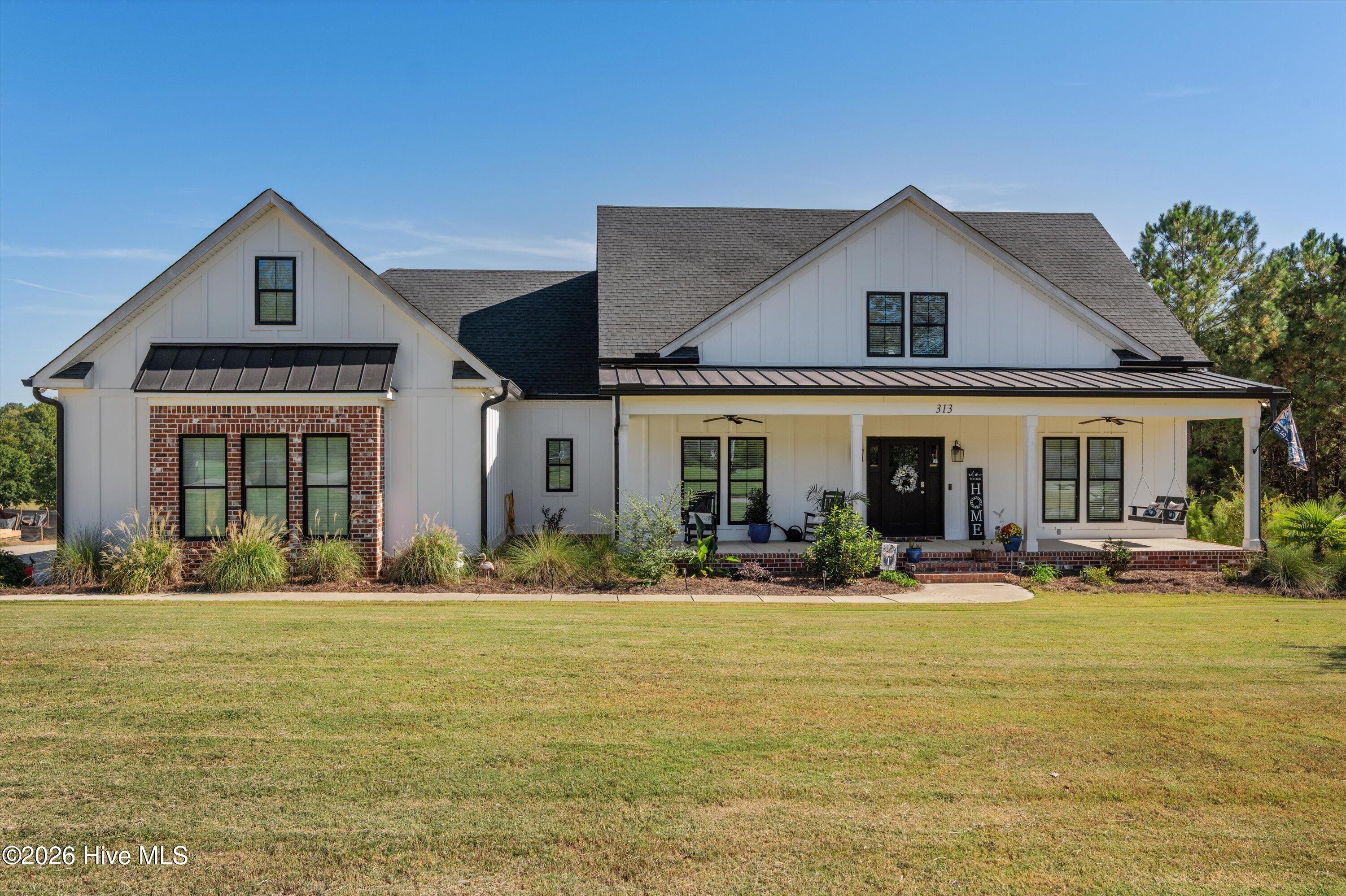 White farmhouse with a wide covered porch, brick accents, and a broad front lawn.