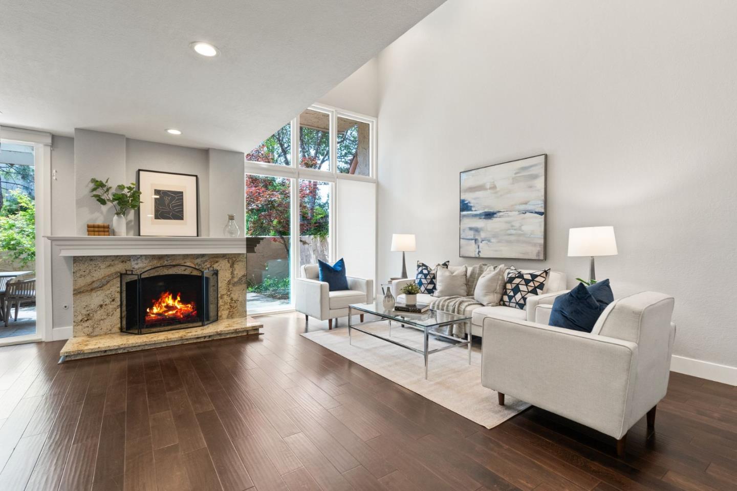 Furnished living room with a stone fireplace, tall windows, and dark wood floors.