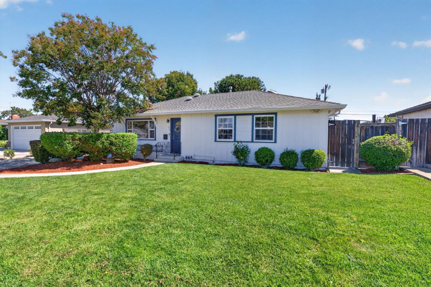 Single-story white house with blue trim, a broad lawn, and flowering tree.