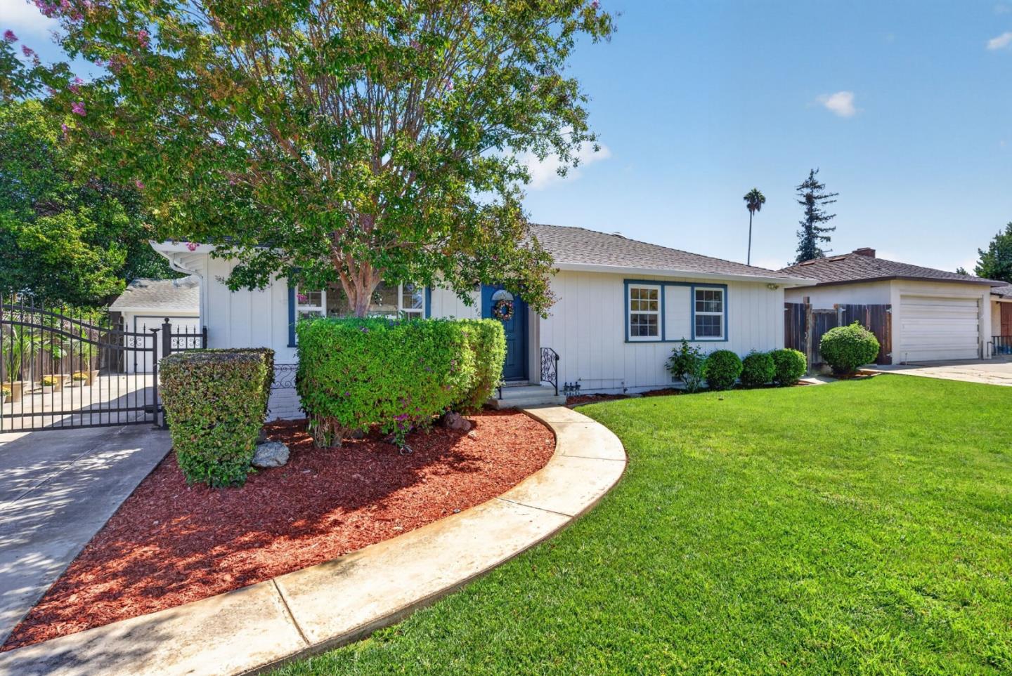 Single-story white home with blue trim, a flowering tree, curved walkway, and landscaped front lawn.