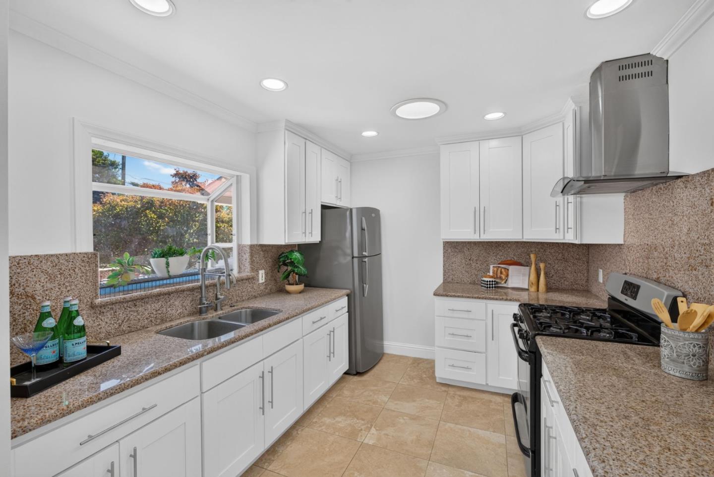 Kitchen with white cabinets, speckled counters, stainless appliances, and a sink beneath a garden-view window.