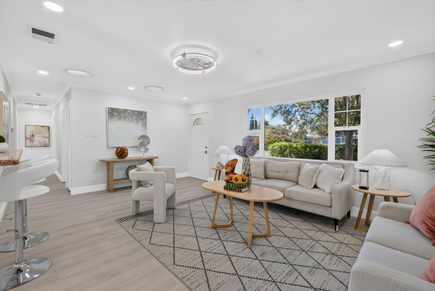 Staged living room with a gray sofa, geometric rug, and large windows overlooking greenery.