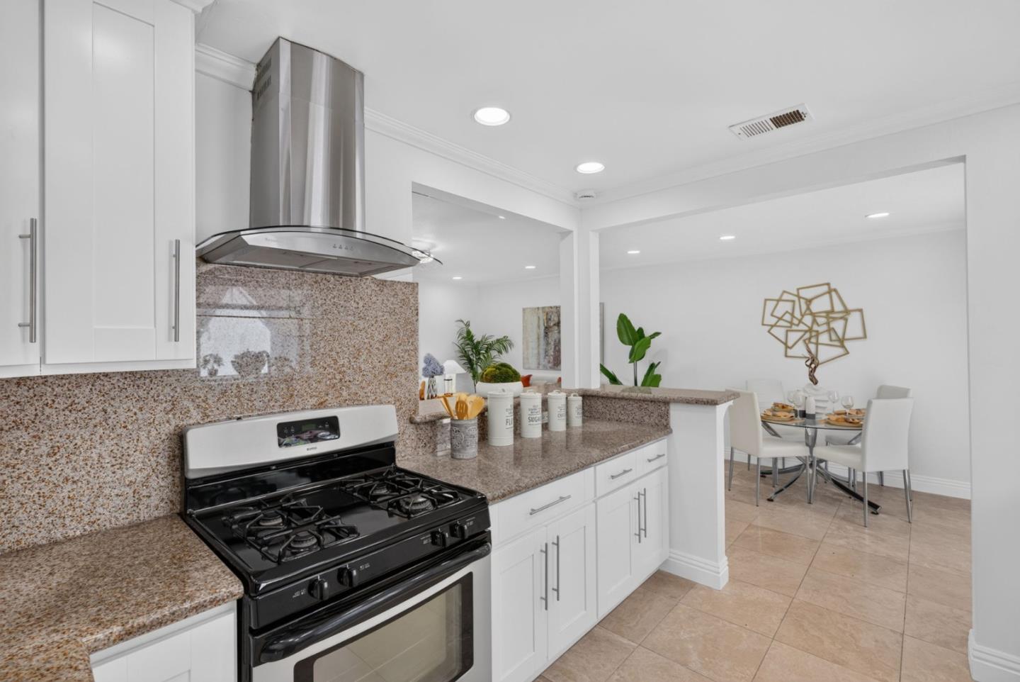Kitchen with granite counters, white cabinetry, and a black gas range opening to a dining area.