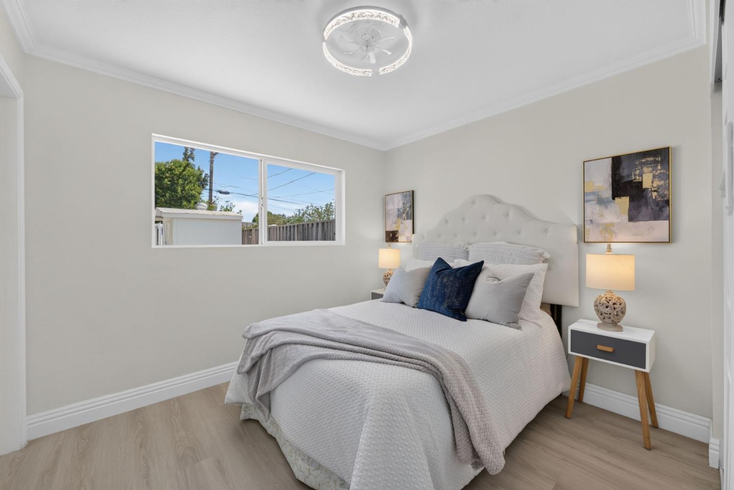 Staged bedroom with a white tufted bed, navy accent pillow, and wide window.