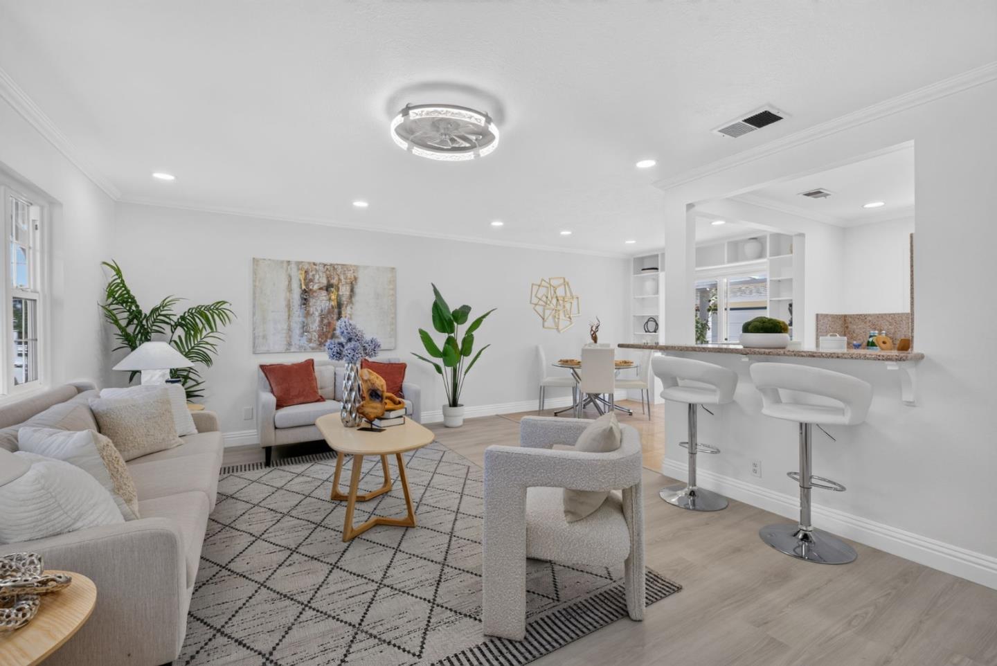 Open-plan living room and kitchen with pale seating, a patterned rug, and a breakfast bar with white stools.
