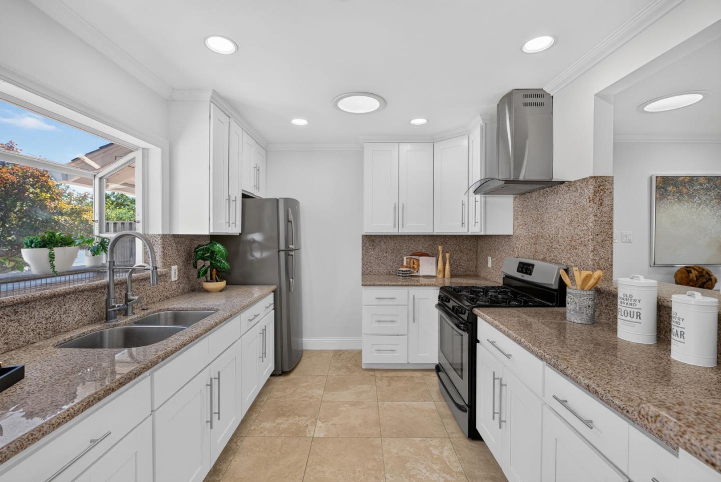 Kitchen with white cabinets, speckled granite counters, and a window above the double-basin sink.