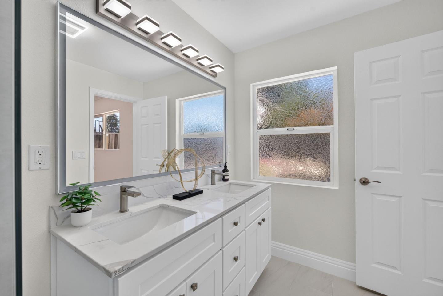 Bathroom with a white double vanity, veined stone countertop, and frosted windows.