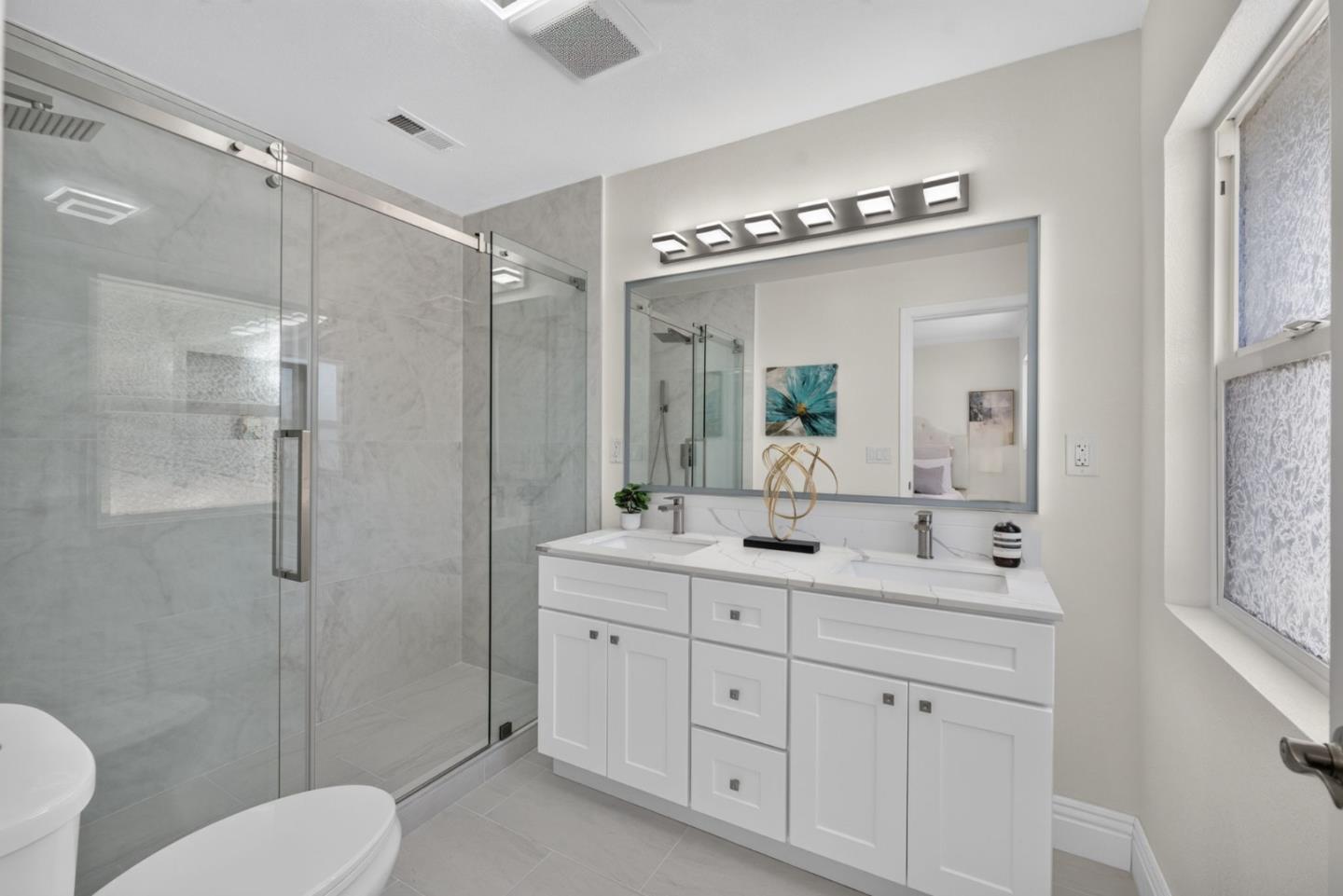 Bathroom with a glass walk-in shower, gray tile, and white double-sink vanity.