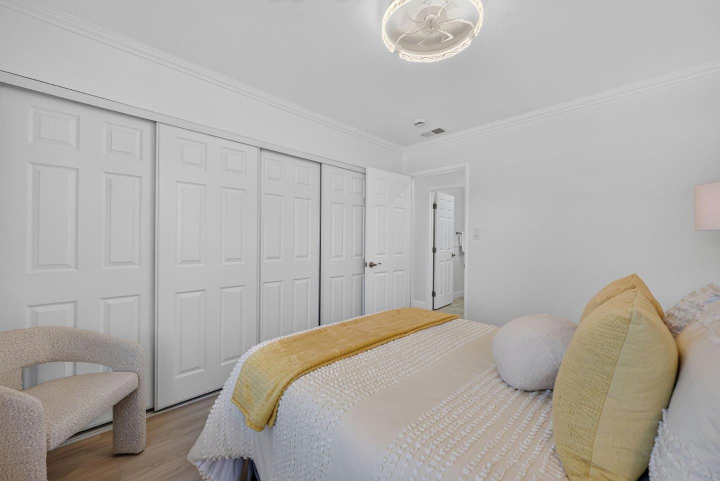 Bedroom with white textured bedding, yellow accents, an upholstered chair, and paneled closet doors.