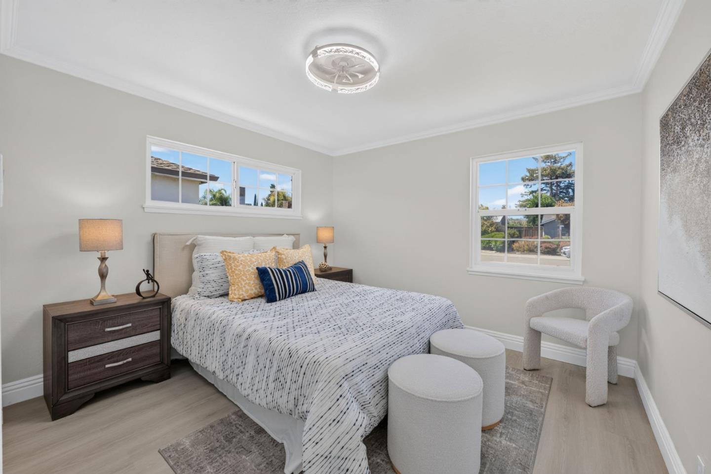 Staged bedroom with patterned white bedding, colorful pillows, and a white accent chair by the window.