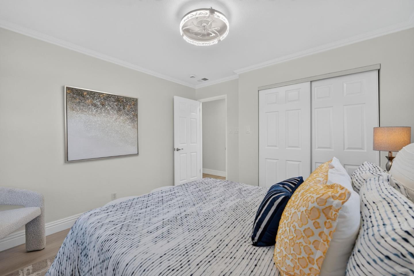 Bedroom with patterned white bedding, yellow and navy pillows, and sliding closet doors.