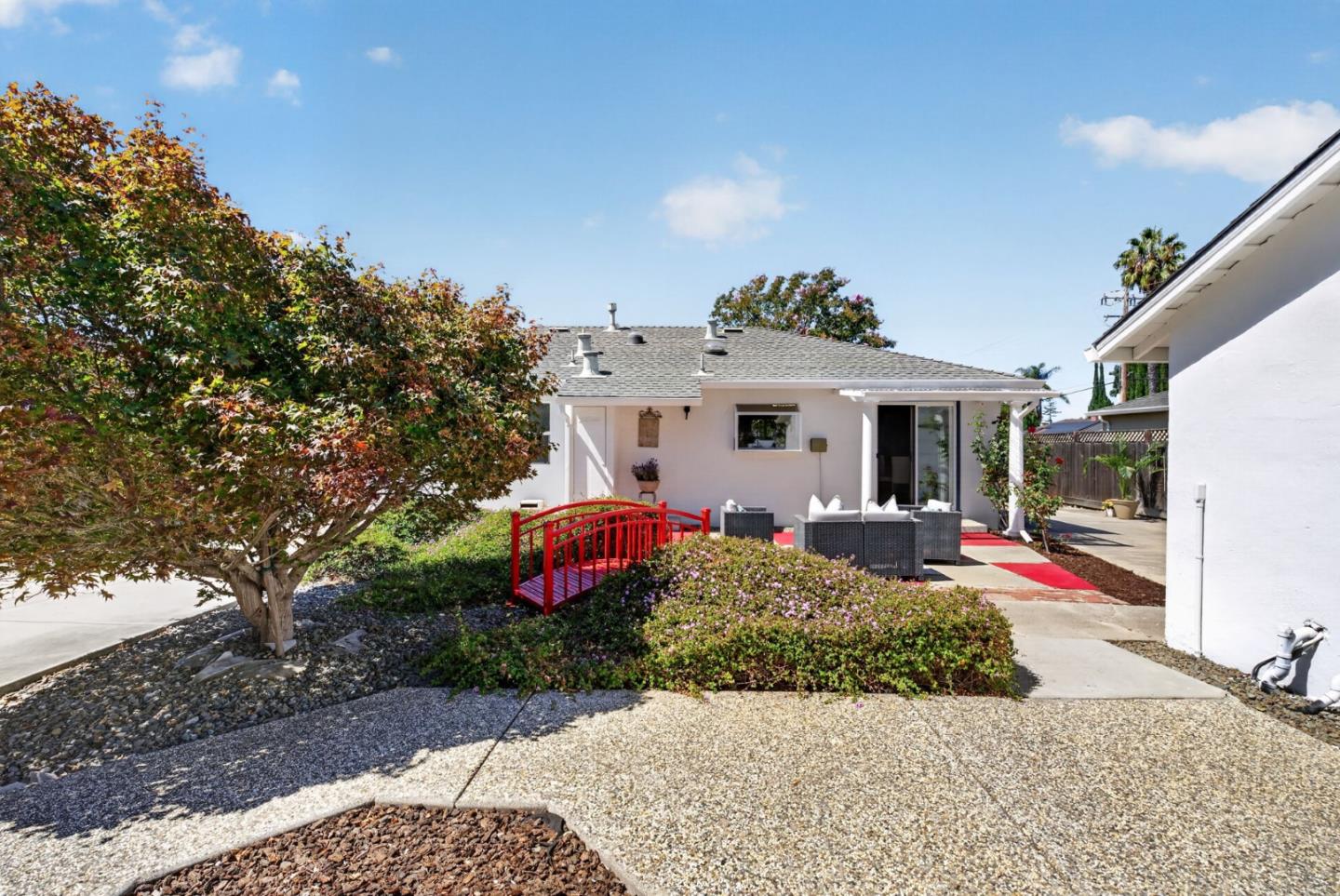 Home’s backyard with a red garden bridge, flowering ground cover, outdoor seating, and paved patio.