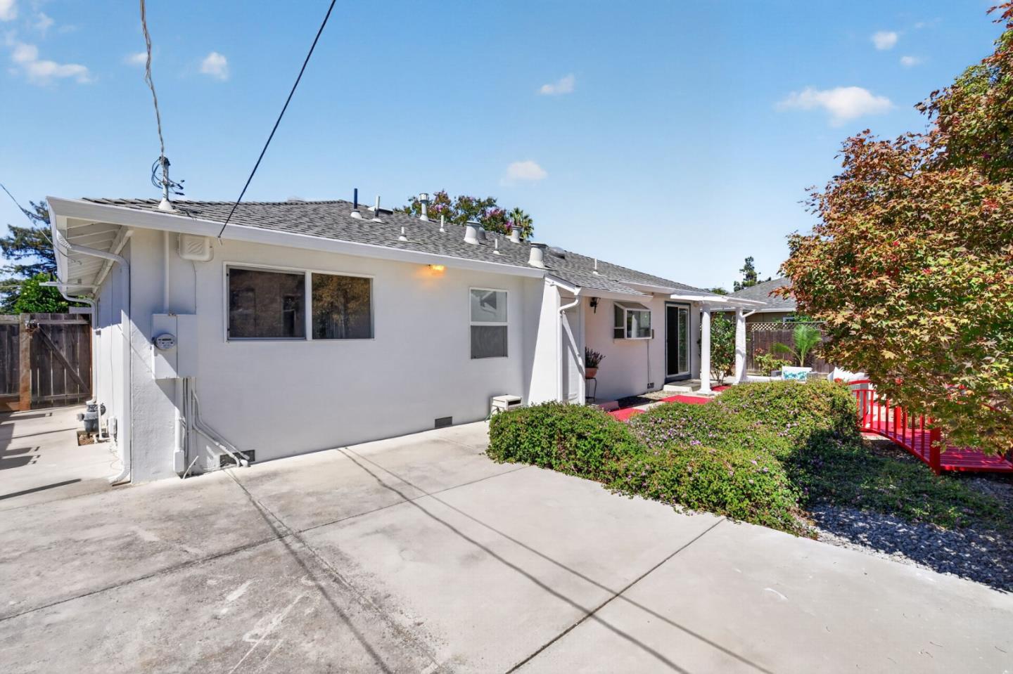 Side and rear of a white single-story house with a wide driveway and red patio deck.
