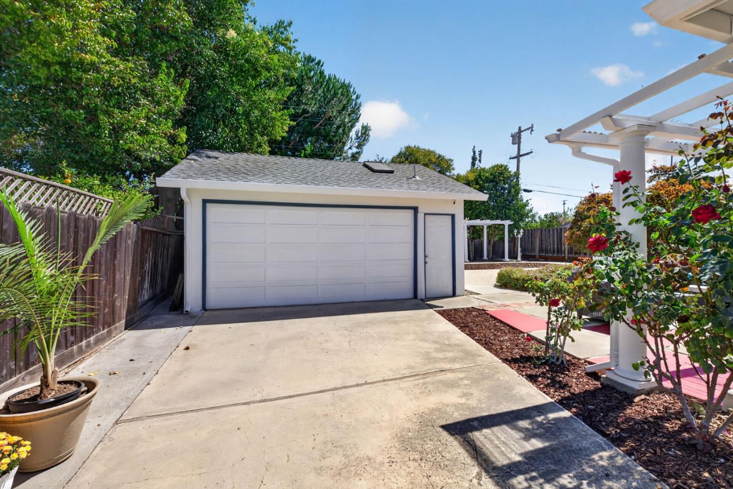 Detached two-car garage and concrete driveway, framed by roses and a white pergola.