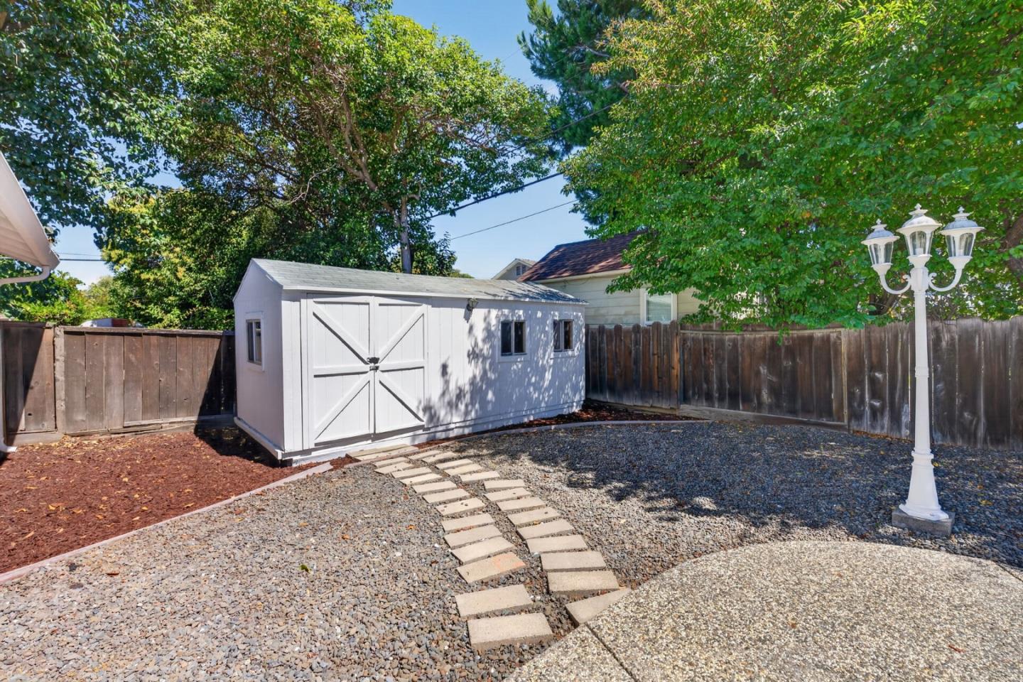Backyard shed beside gravel landscaping, stepping stones, and a white lamp post.
