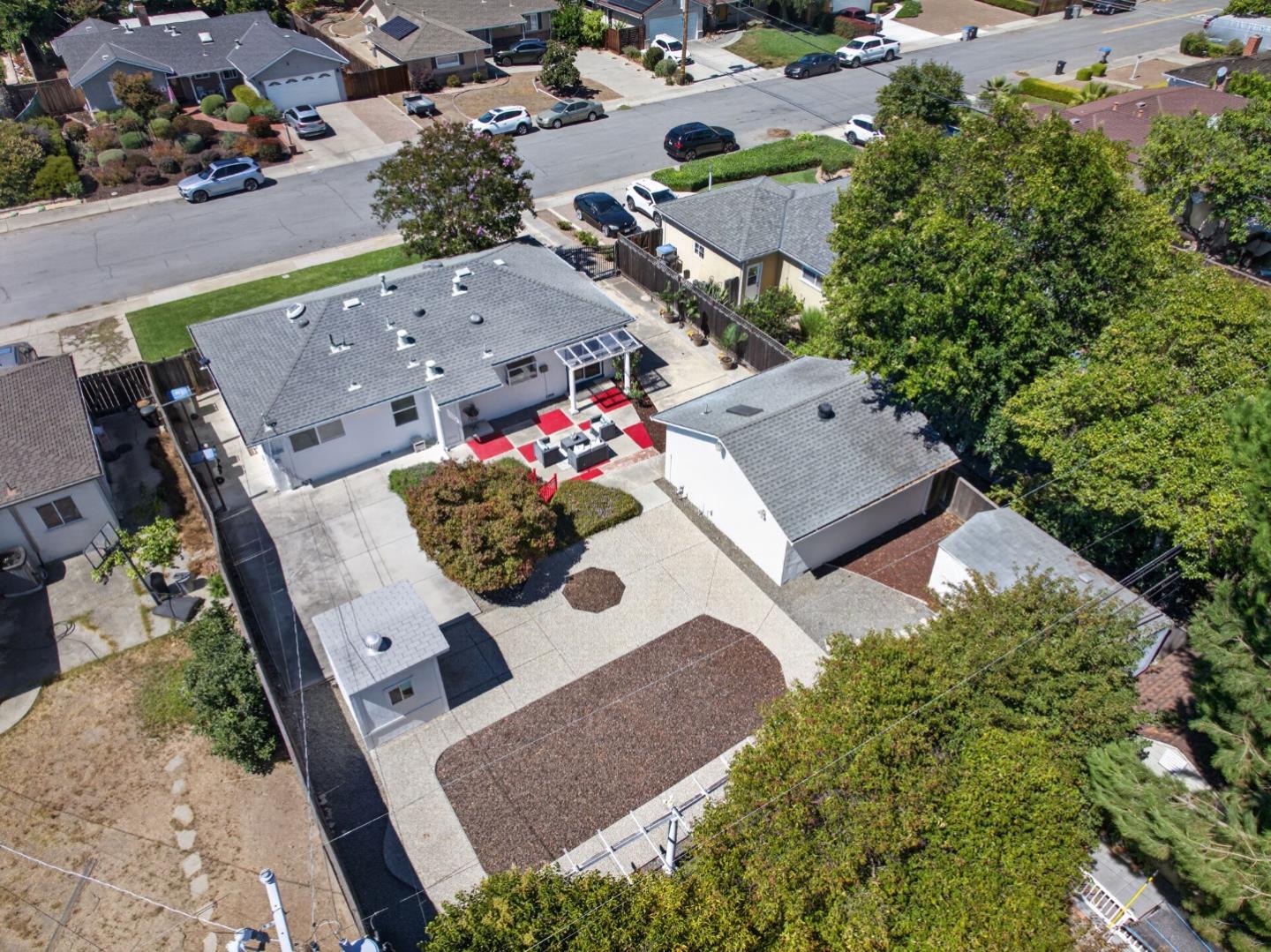 Aerial view of the home’s paved backyard, outdoor dining area, and surrounding neighborhood.