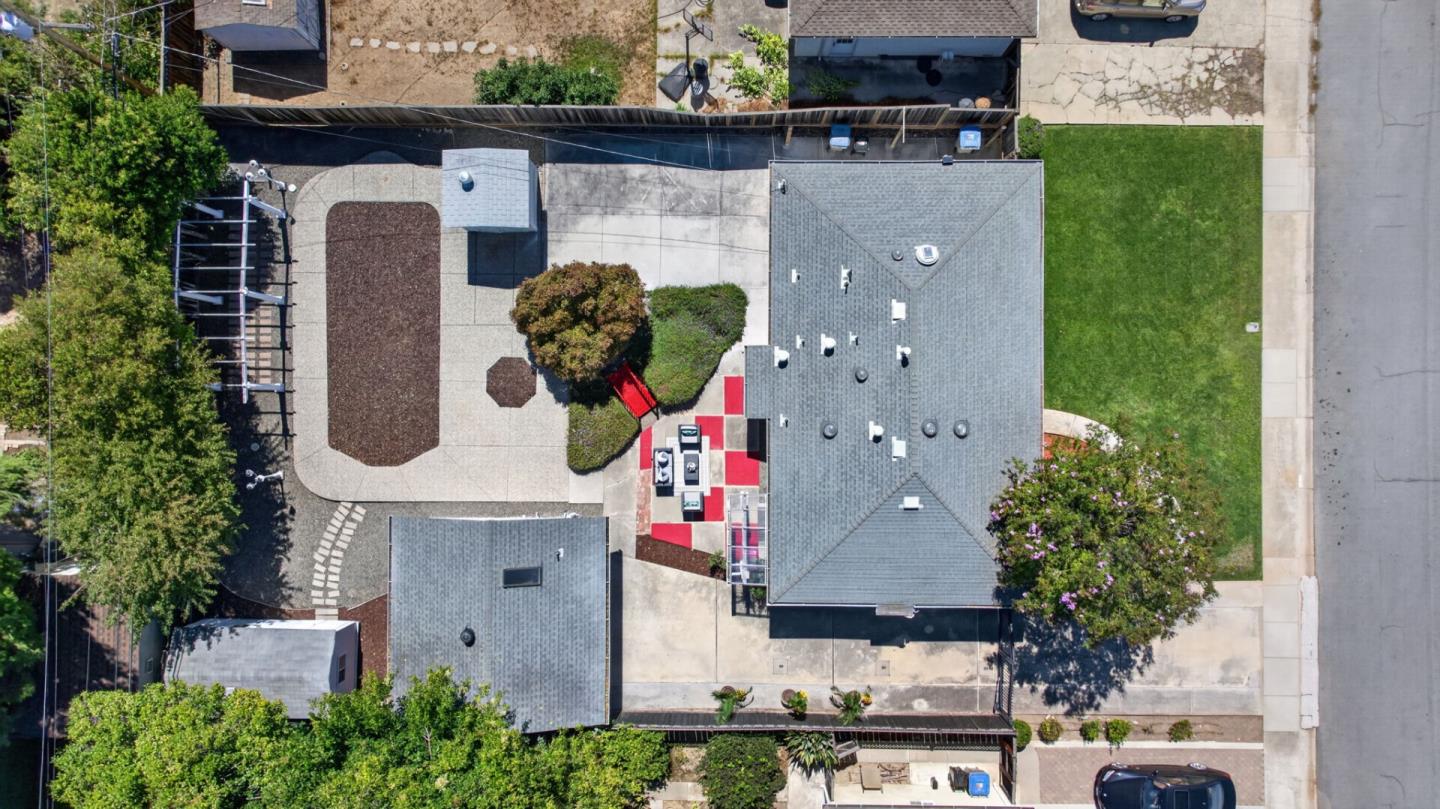 Aerial view of a home with a paved courtyard, green lawn, and red-and-white patio area.