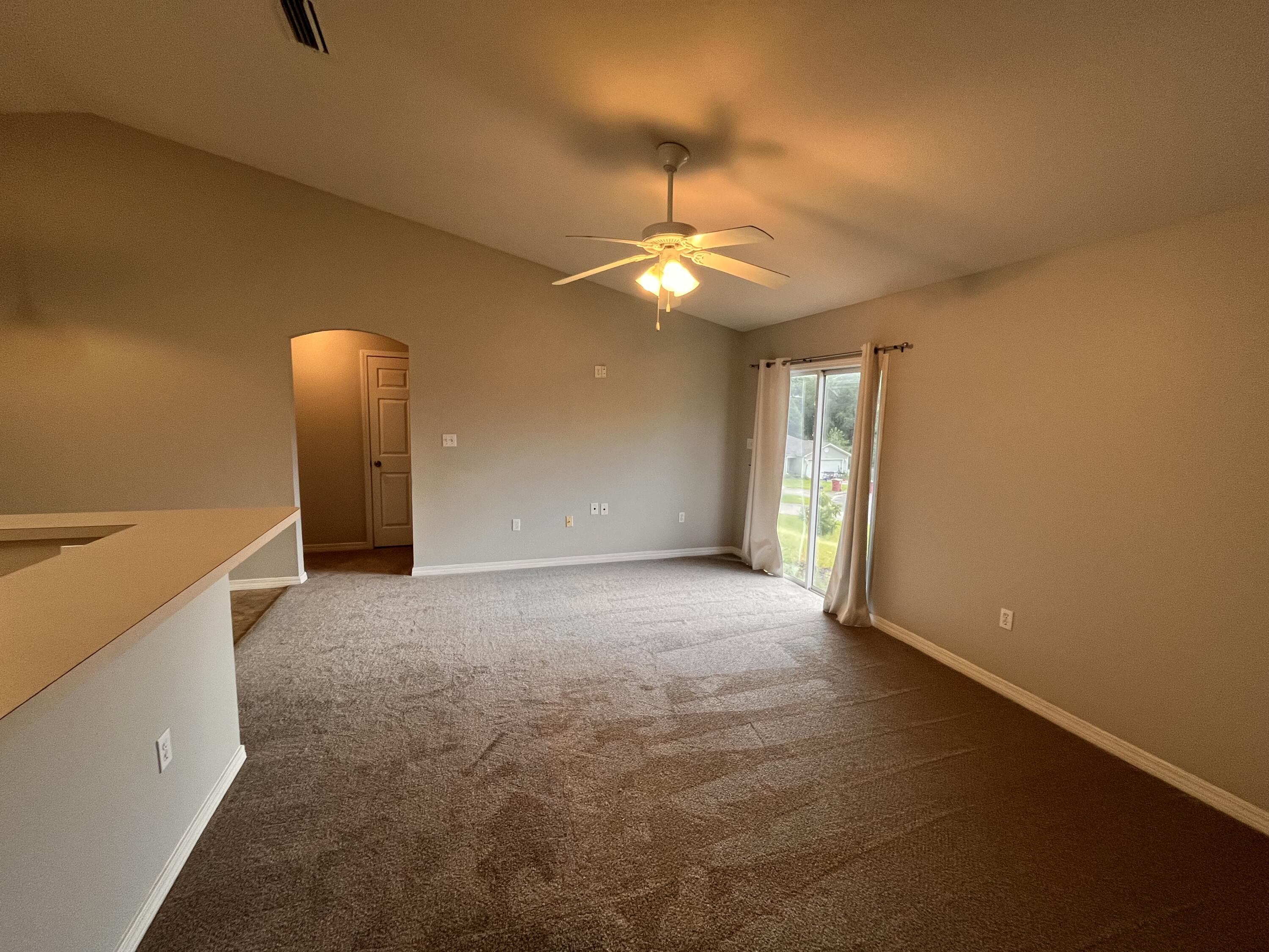 Unfurnished living room with brown carpet, ceiling fan, and sliding glass door.