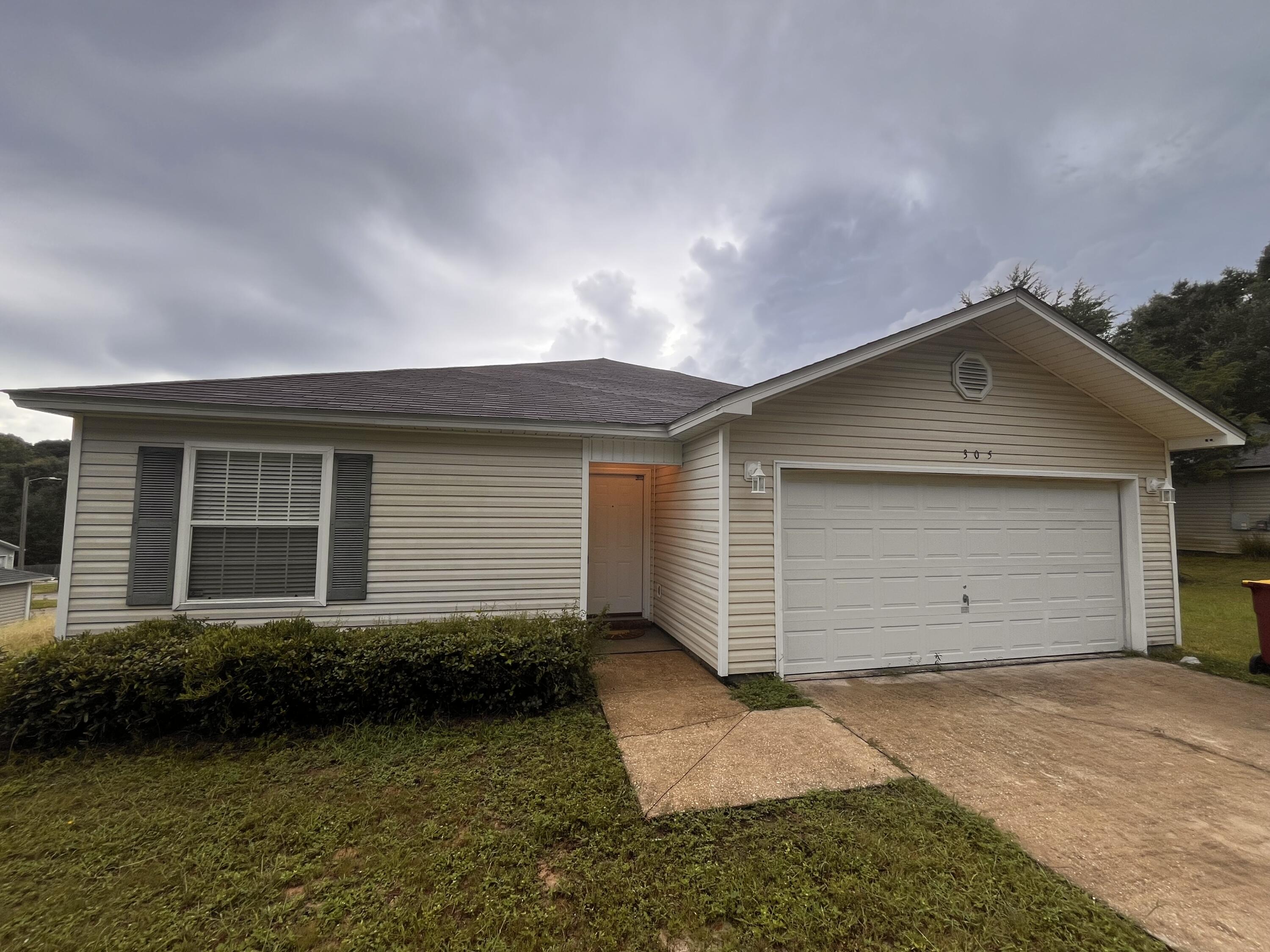 Single-story beige house with a double garage, shuttered window, and concrete driveway.