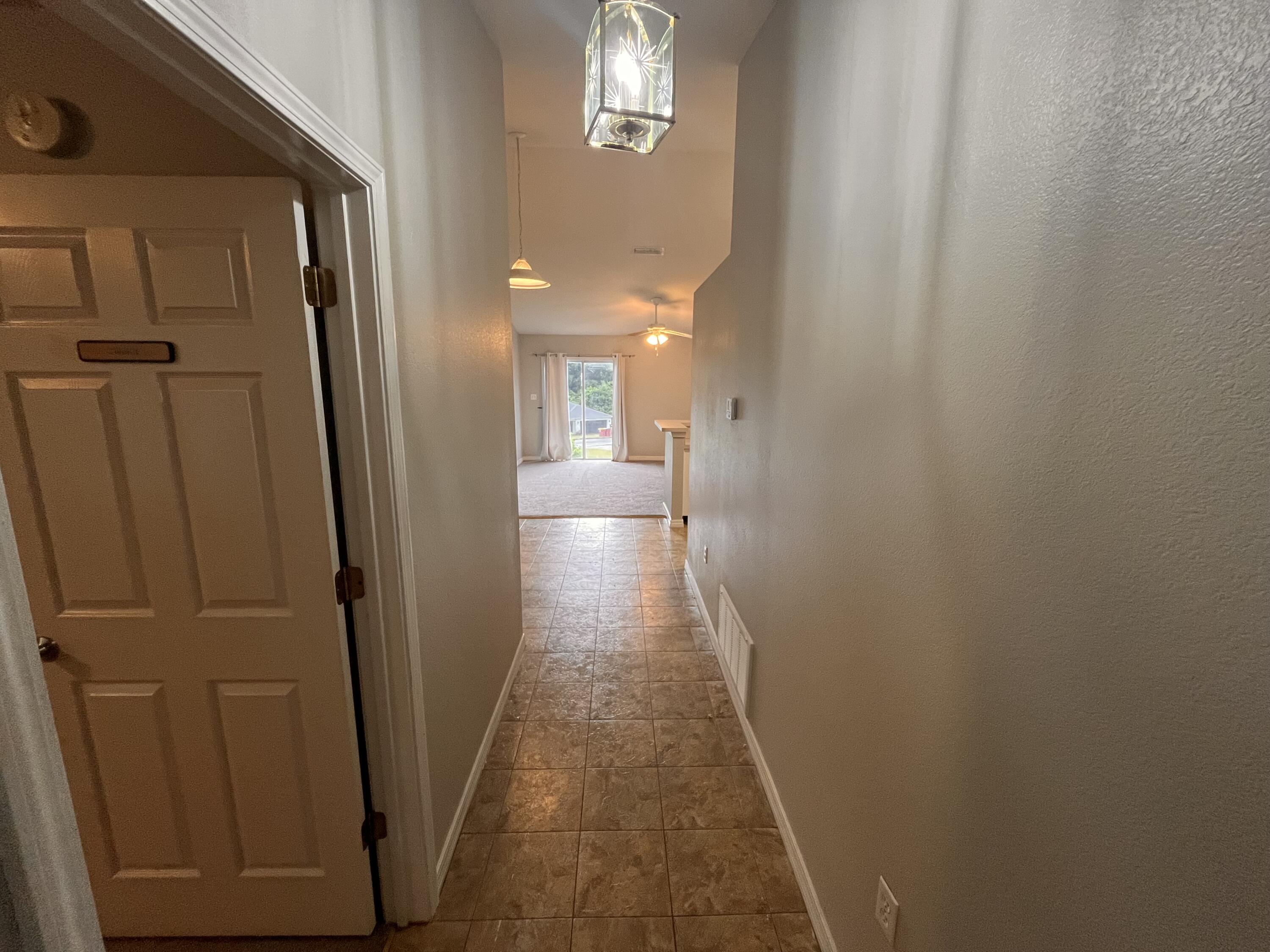 Tiled entry hallway leading to a carpeted living area with sliding glass doors.