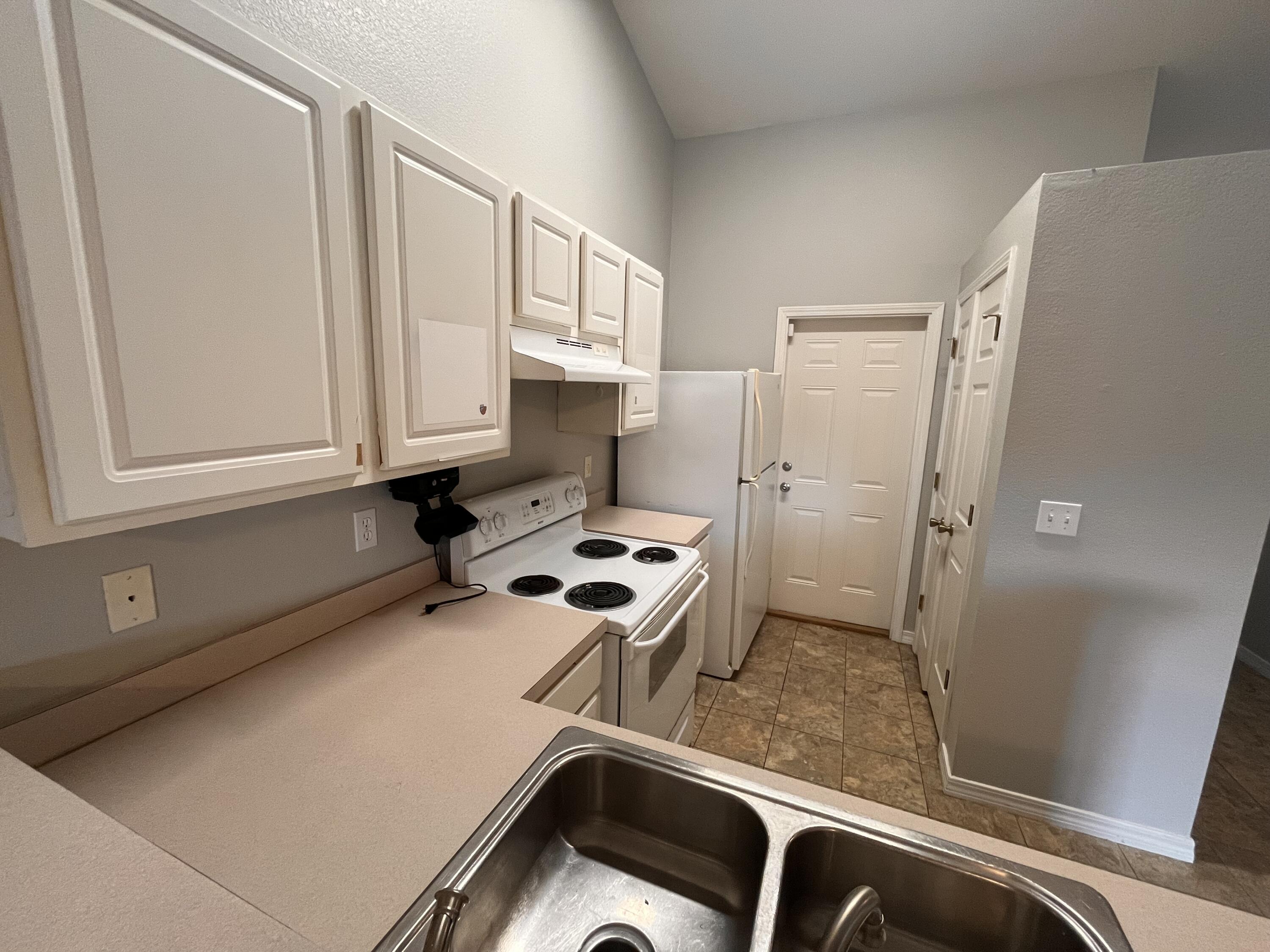 Kitchen with white cabinets and appliances, beige counters, and a stainless steel double-basin sink.