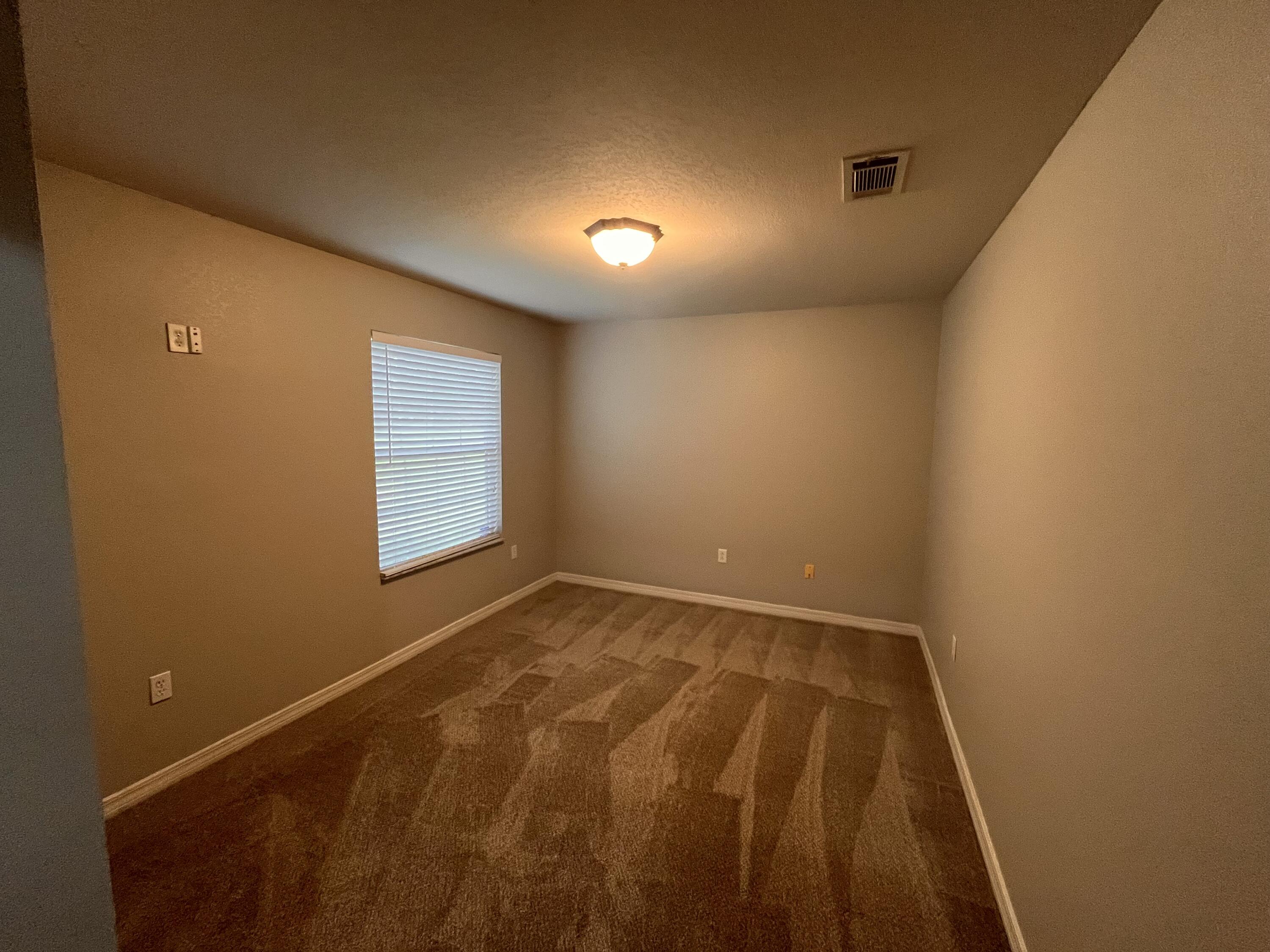 Empty room with patterned brown carpet and a window with closed blinds.