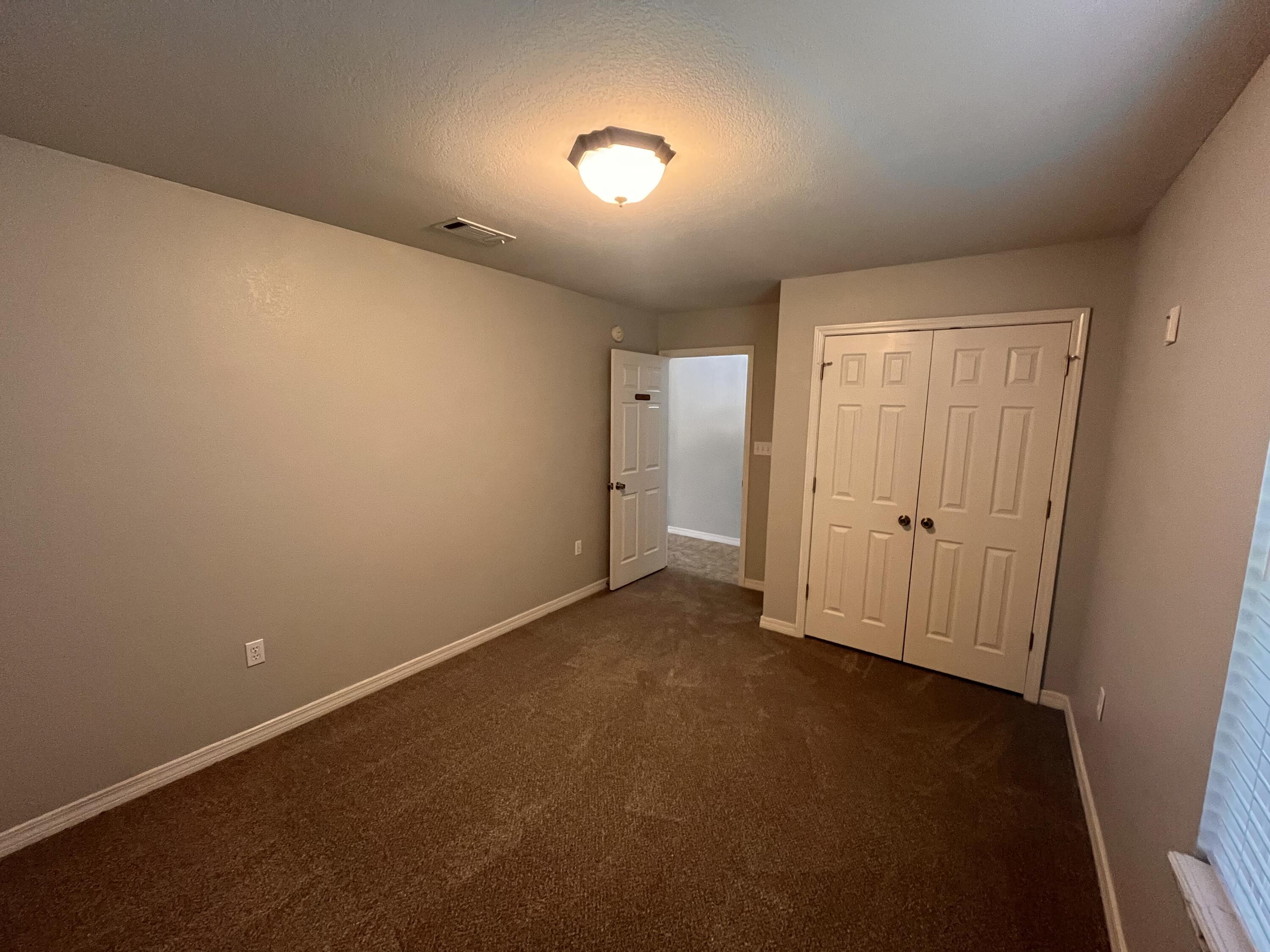 Empty carpeted room with beige walls, white double closet doors, and an open doorway.
