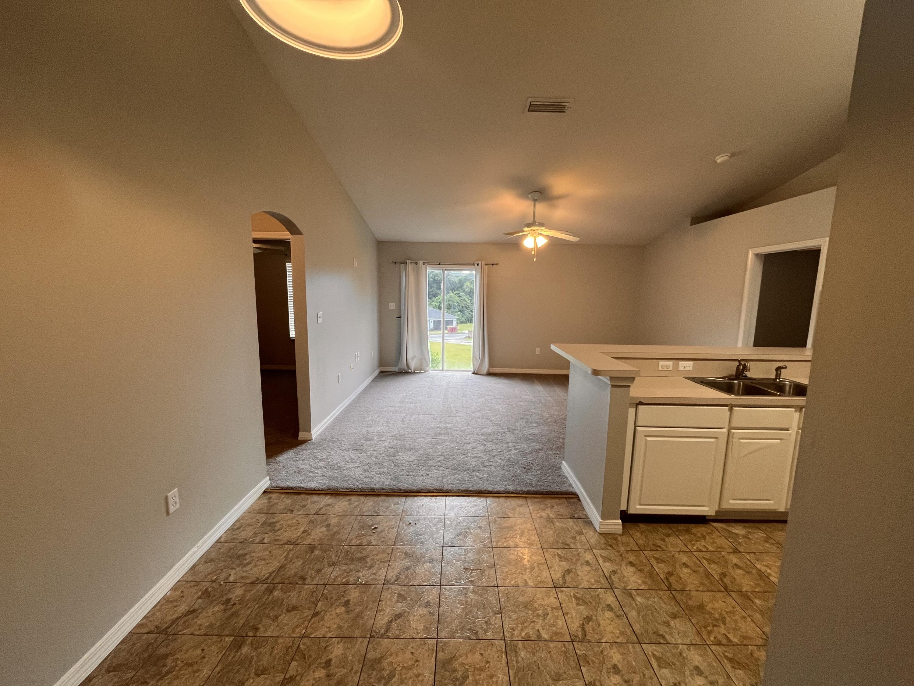 Open-plan living area with gray carpet, tiled kitchen peninsula, and sliding glass doors to the yard.