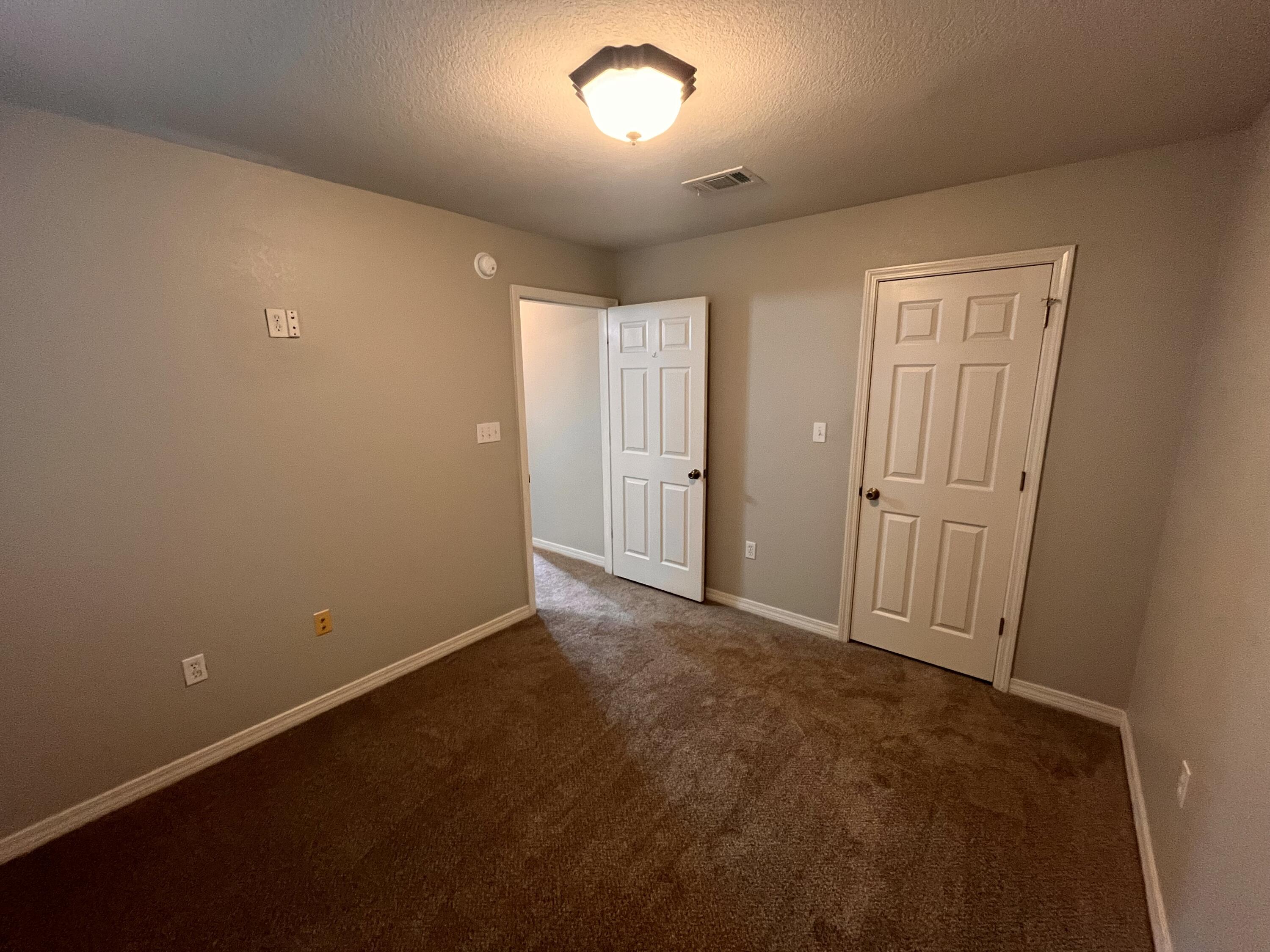 Empty carpeted room with beige walls and two white doors, one standing open.