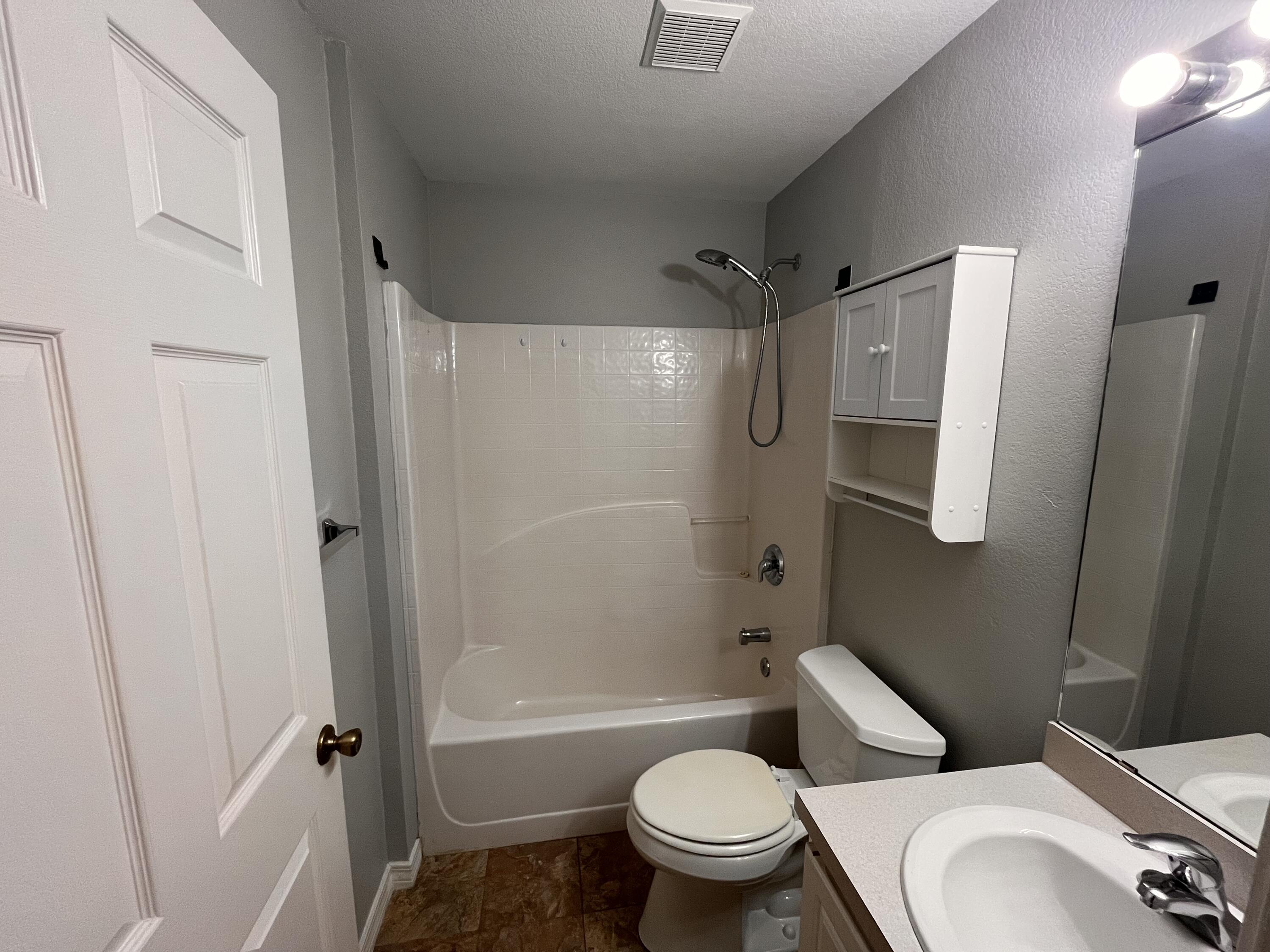 Bathroom with a tiled tub and shower, toilet, and vanity with a large mirror.