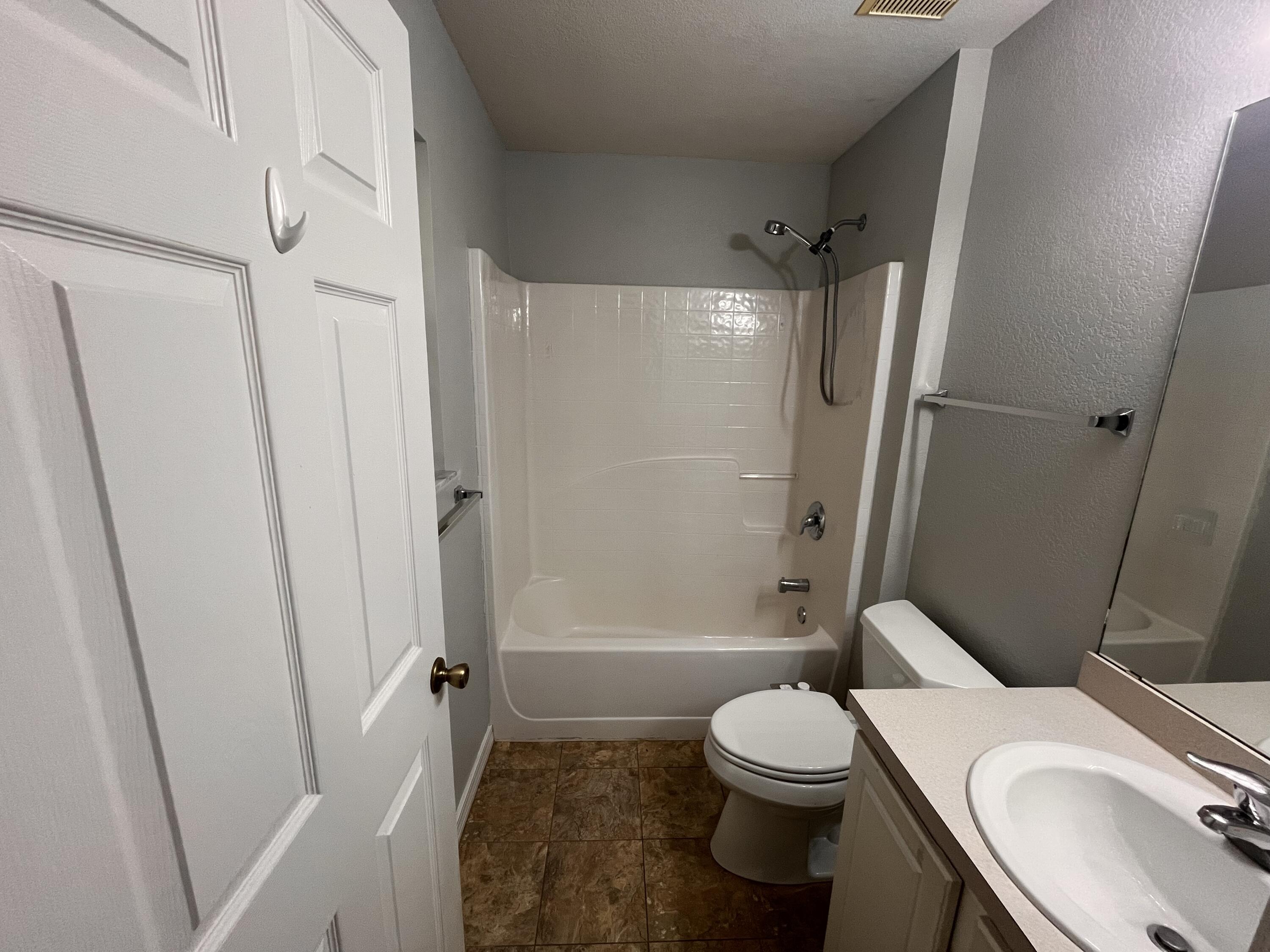 Bathroom with a white tub and shower, toilet, single-sink vanity, and brown tile floor.