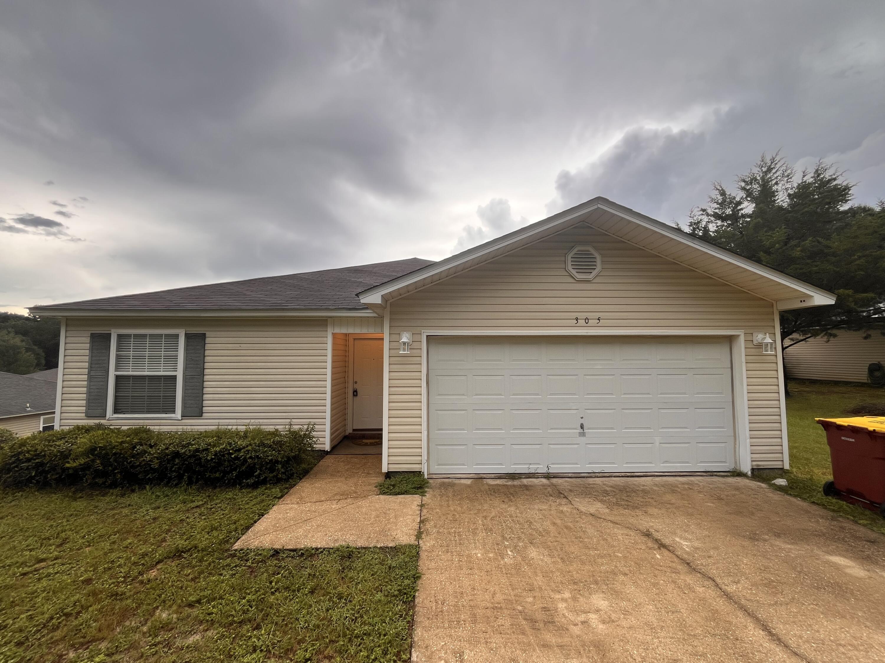 Beige single-story house with a white double garage, covered entry, and broad concrete driveway.