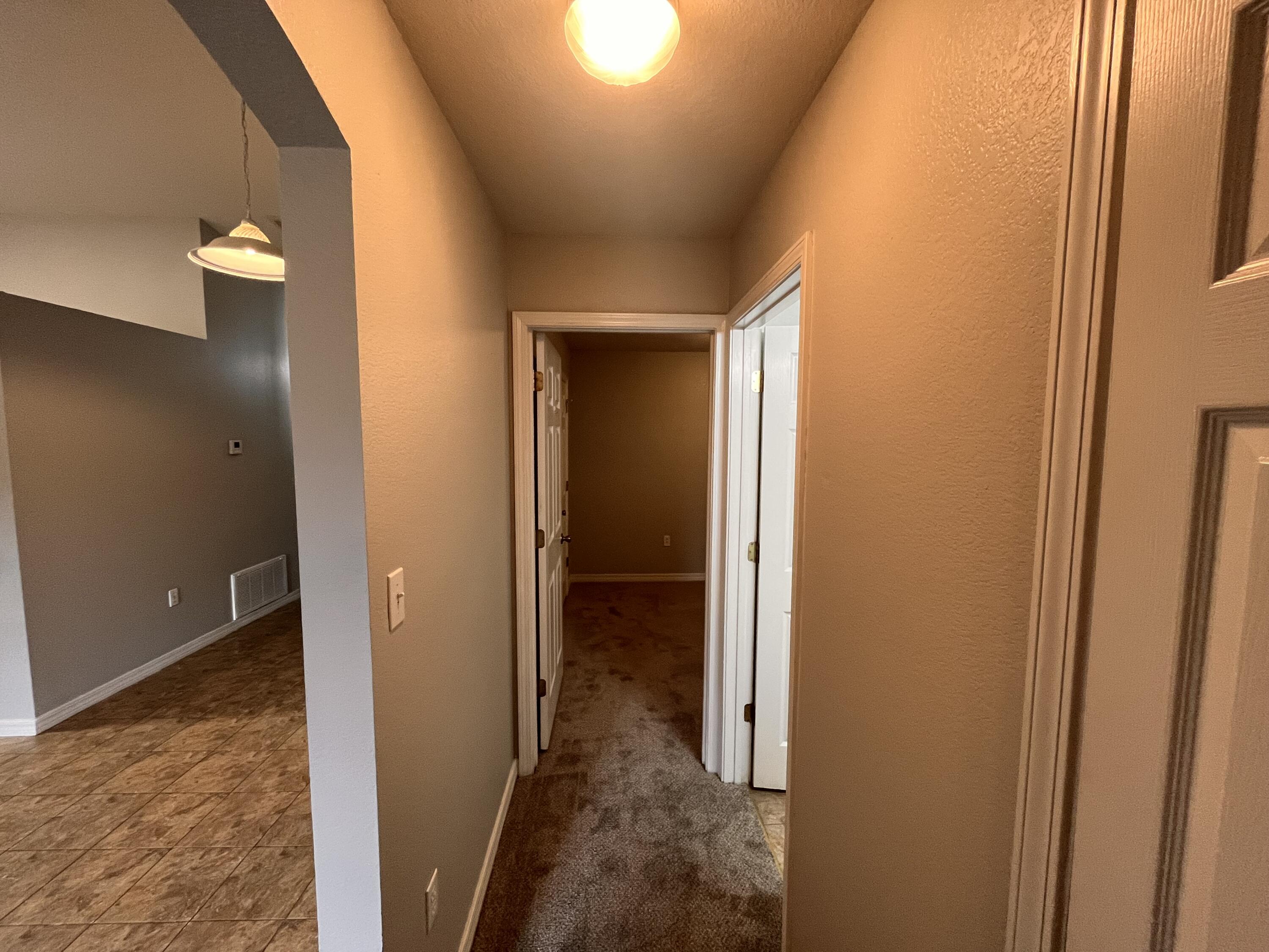 Carpeted hallway with open doorways and a tiled room visible to the left.