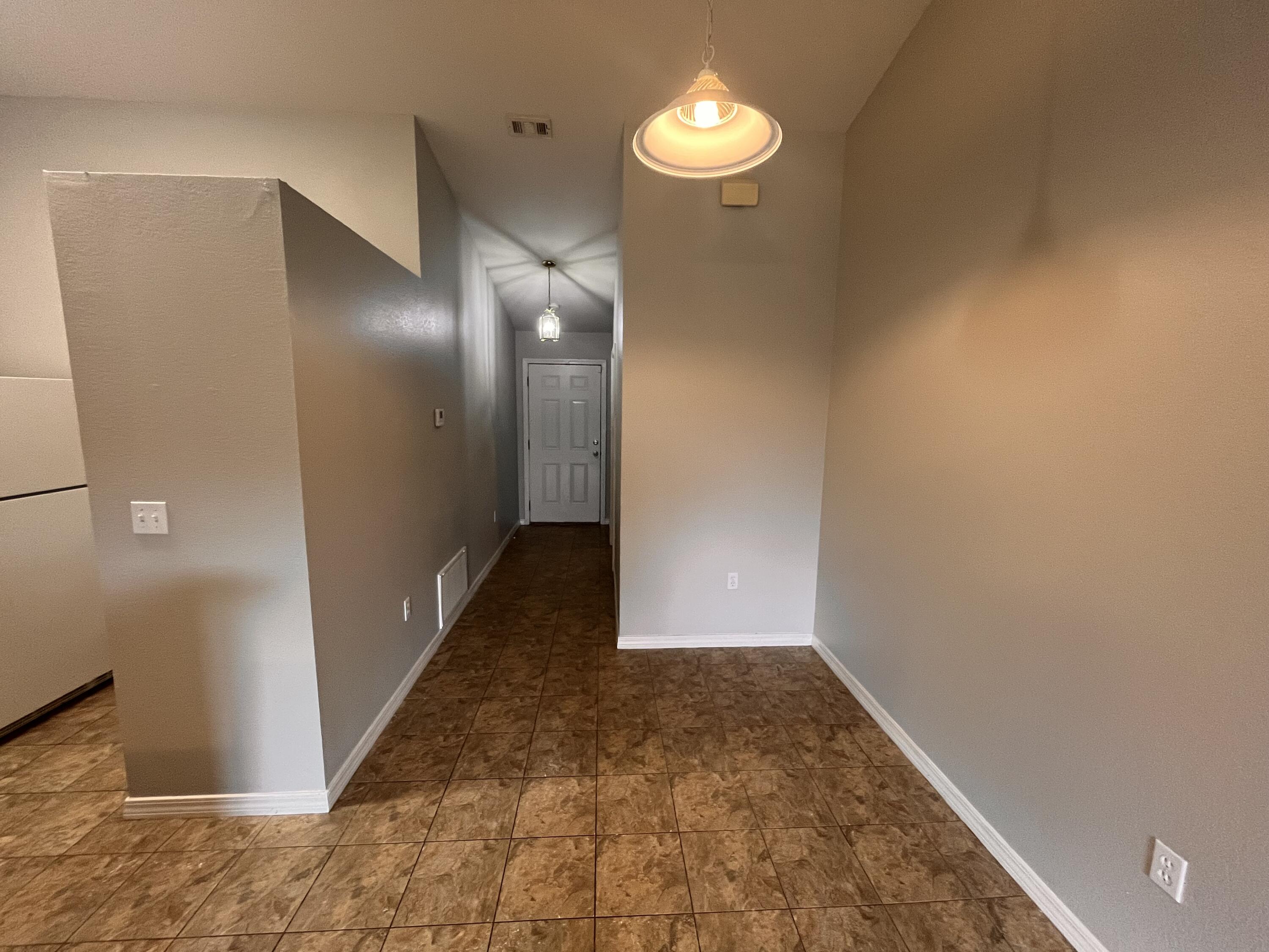 Empty entryway with brown patterned tile flooring and a hallway leading to the front door.