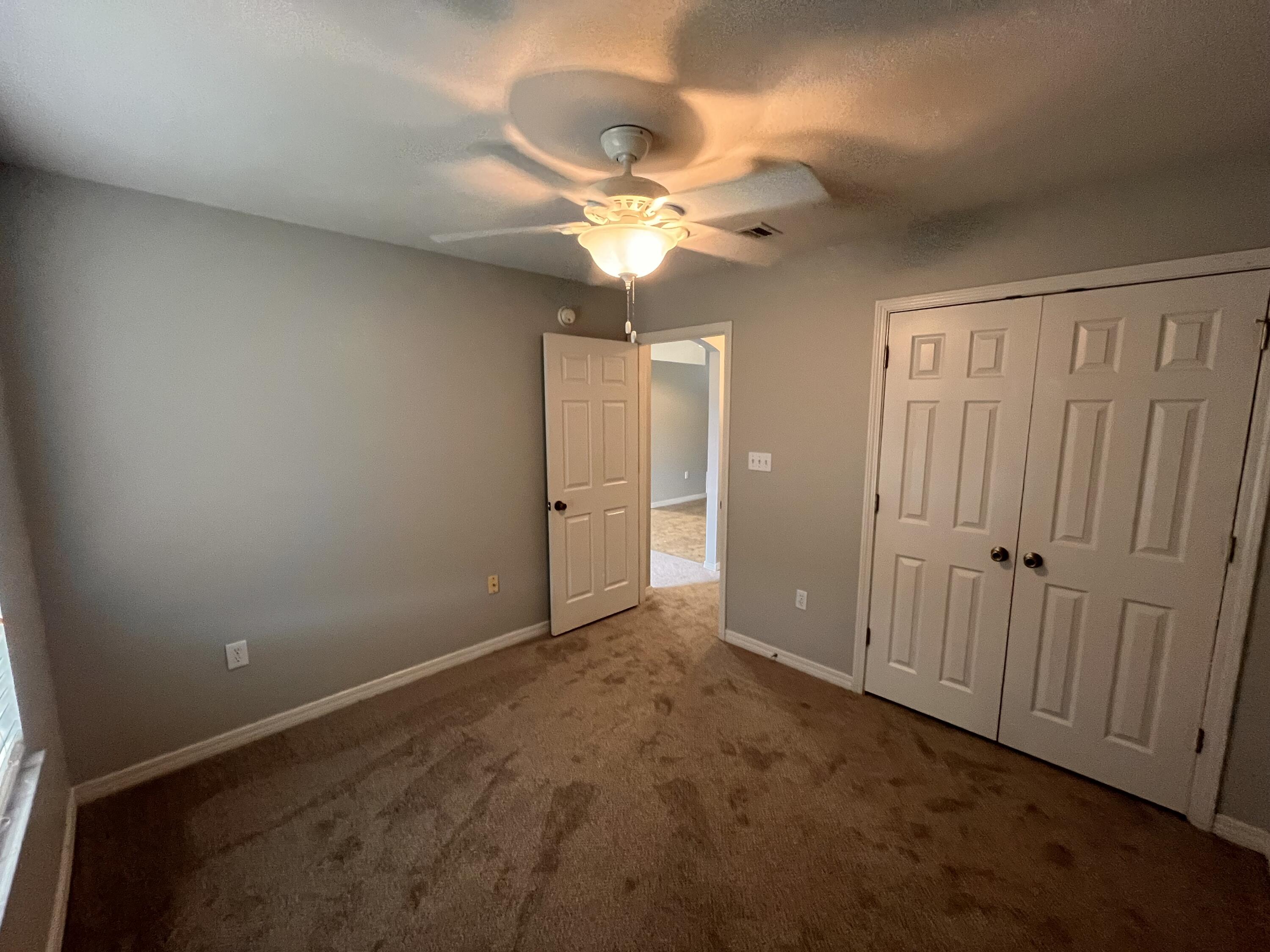 Empty bedroom with beige carpet, a ceiling fan, and double closet doors.