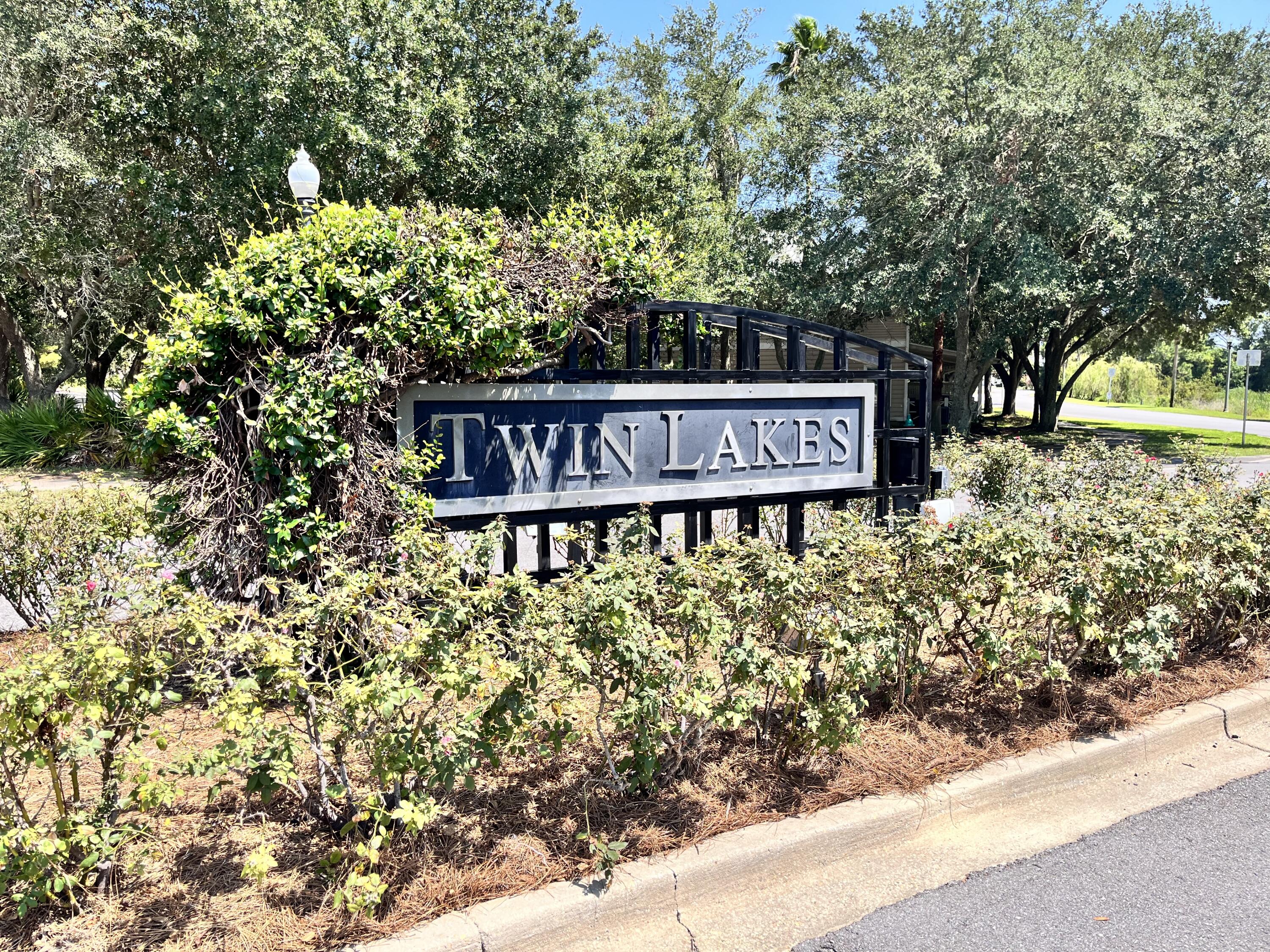 Twin Lakes entrance sign surrounded by shrubs and mature trees.