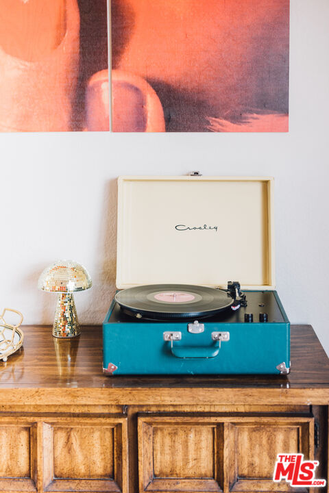 Turquoise record player on a carved wooden console beneath abstract artwork, with a mosaic lamp beside it.