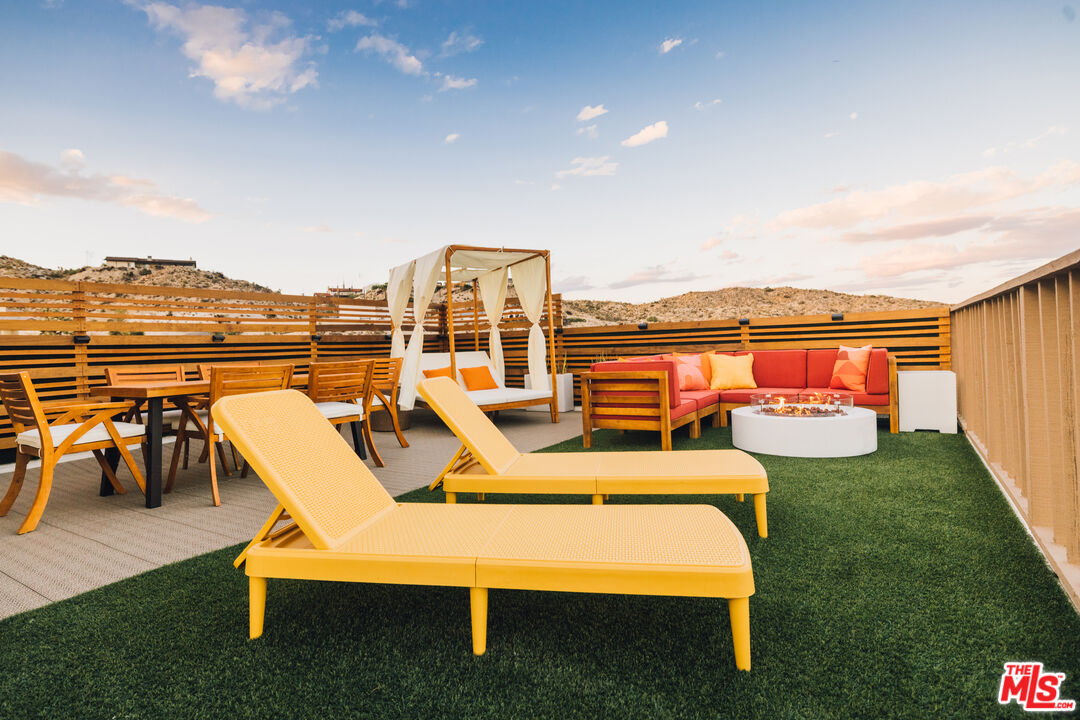 Furnished patio with yellow chaise lounges and a fire pit, overlooking desert hills.