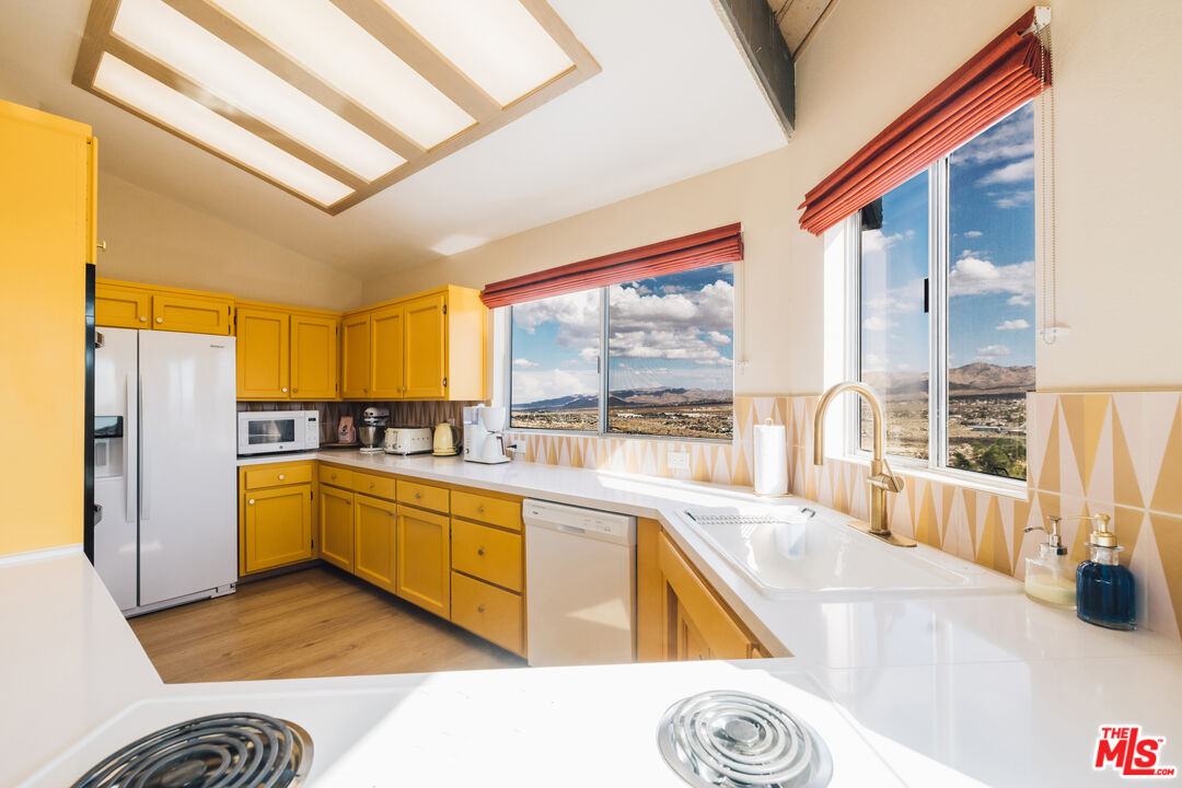Kitchen with yellow cabinets and white counters, overlooking a desert valley and distant mountains.
