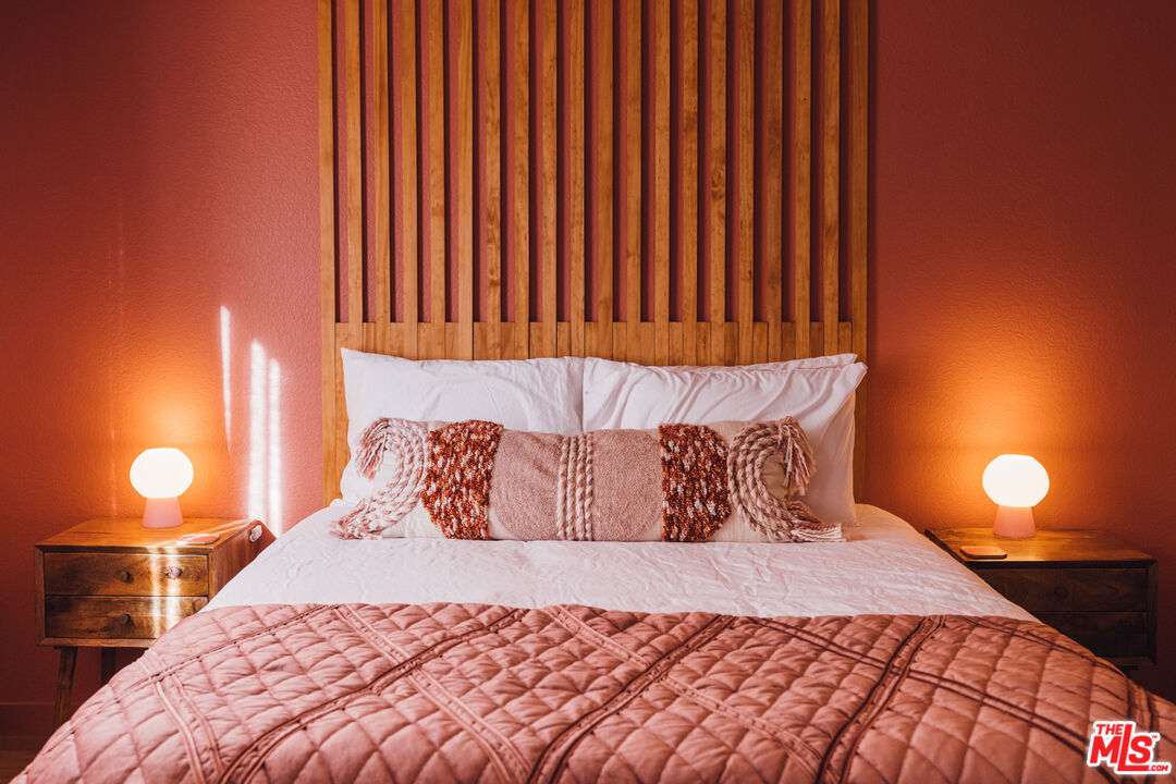 Bedroom with white bedding, a quilted rust-colored coverlet, and glowing bedside lamps.