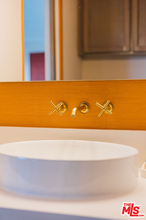 White vessel sink with gold wall-mounted faucet and warm wood backsplash.