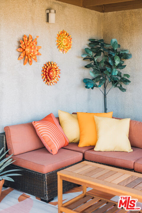 Covered patio with a salmon wicker sectional, colorful pillows, wooden coffee table, and metal flower wall decor.