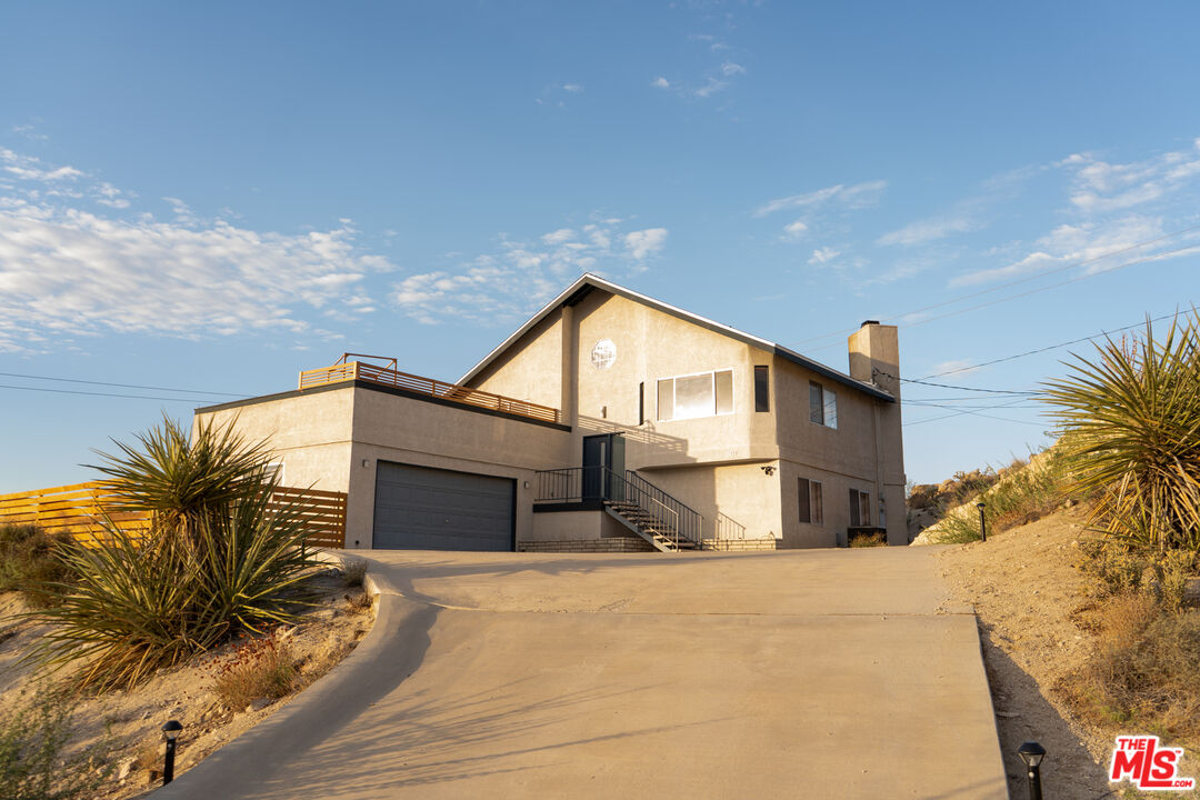 Two-story stucco home with a broad driveway, garage, and rooftop terrace in a desert landscape.